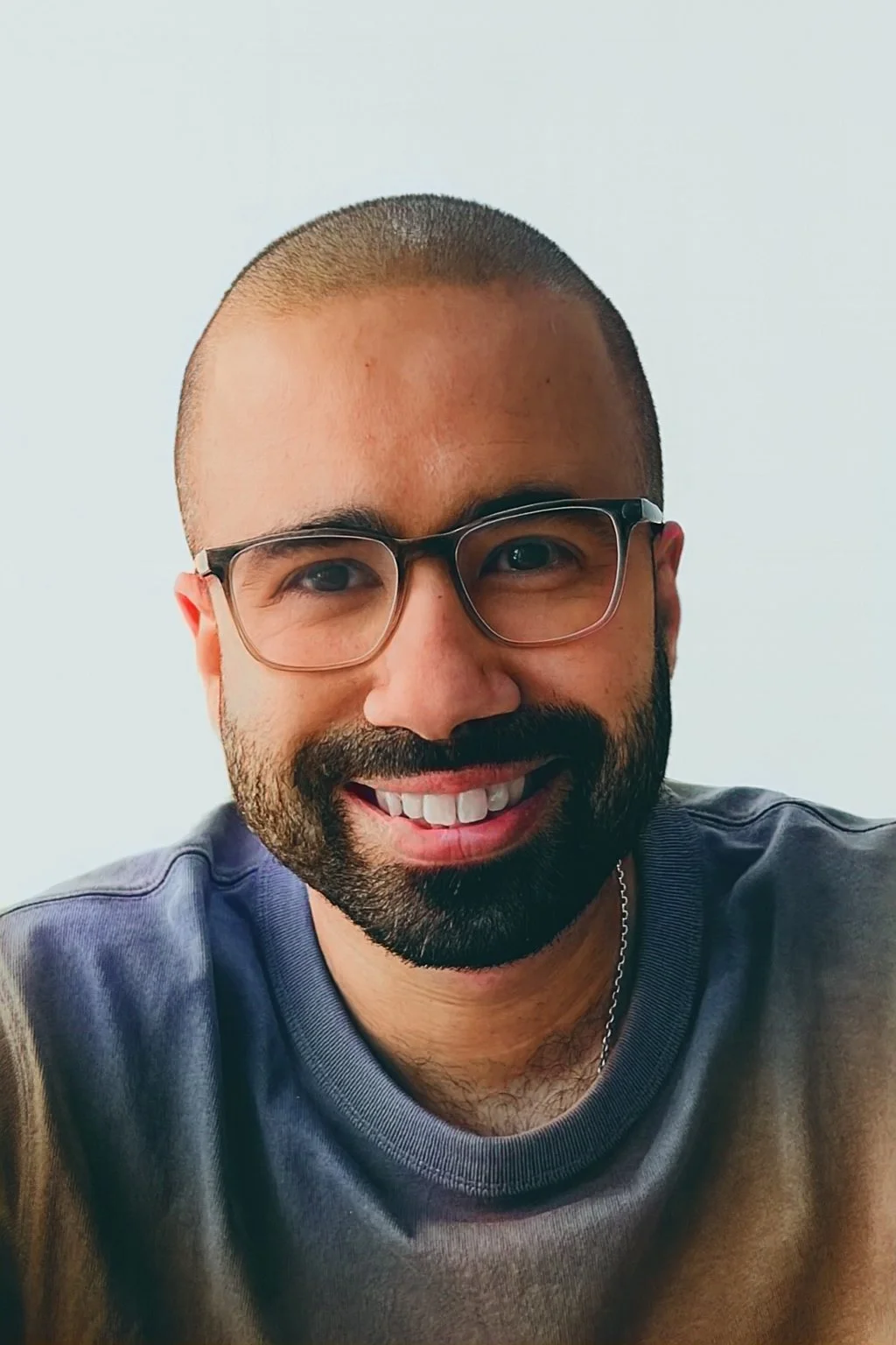 A smiling man with glasses and a beard, wearing a gray shirt.
