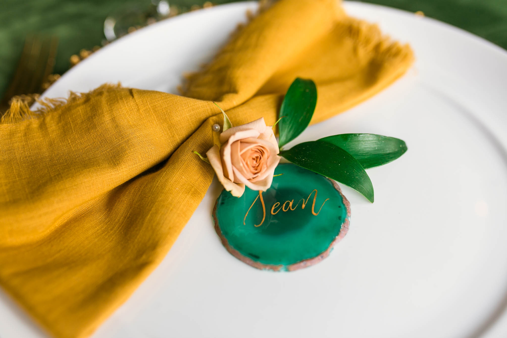 Place setting for a Wedding Guest Table with a Green Velvet Table Cloth, Yellow Napkin and Gold Flatware with Emerald Agate Name Sign and gold calligraphy - oahu hawaii wedding photography