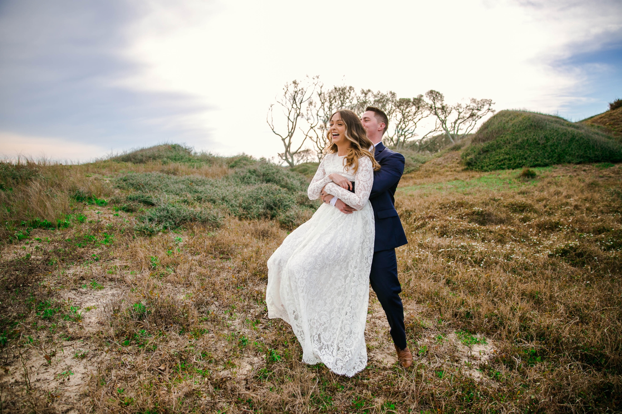 Groom swinging his bride around in Lush Green Grass - Beach Elopement Photography - wedding dress by asos with purple and pink flowers and navy suit - oahu hawaii wedding photographer