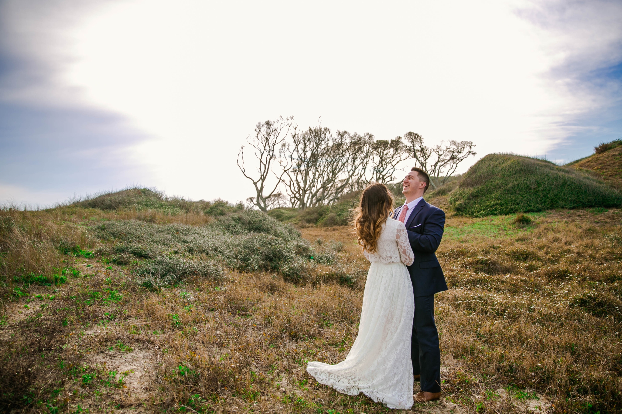Bride and groom laughing in Lush Green Hills - Beach Elopement Photography - wedding dress by asos with purple and pink flowers and navy suit - oahu hawaii wedding photographer