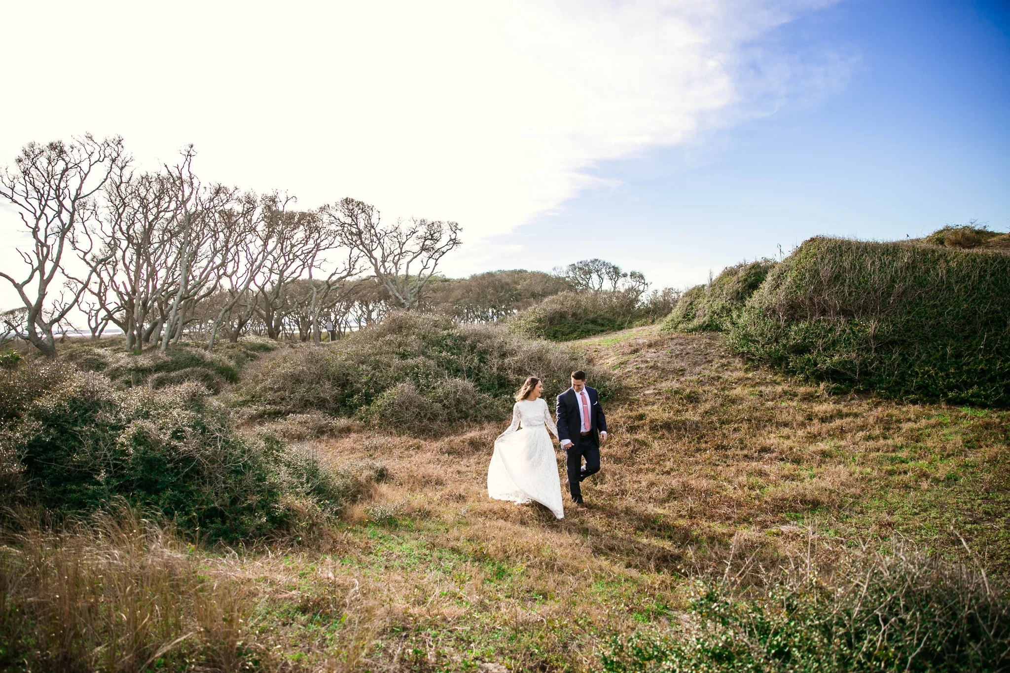 Bride and Groom walking in Lush Green Hills - Beach Elopement Photography - wedding dress by asos with purple and pink flowers and navy suit - oahu hawaii wedding photographer