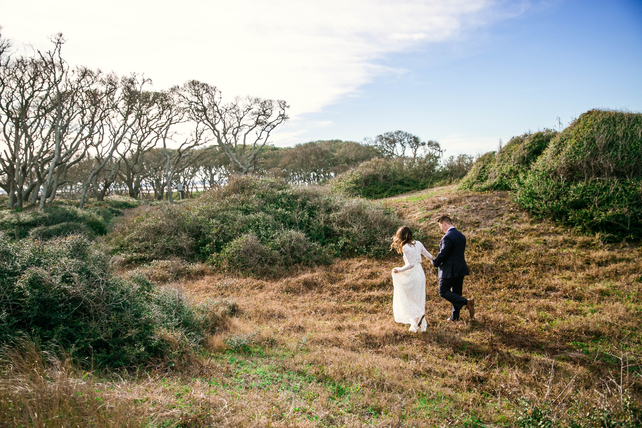 Bride and Groom walking in Lush Green Hills - Beach Elopement Photography - wedding dress by asos with purple and pink flowers and navy suit - oahu hawaii wedding photographer
