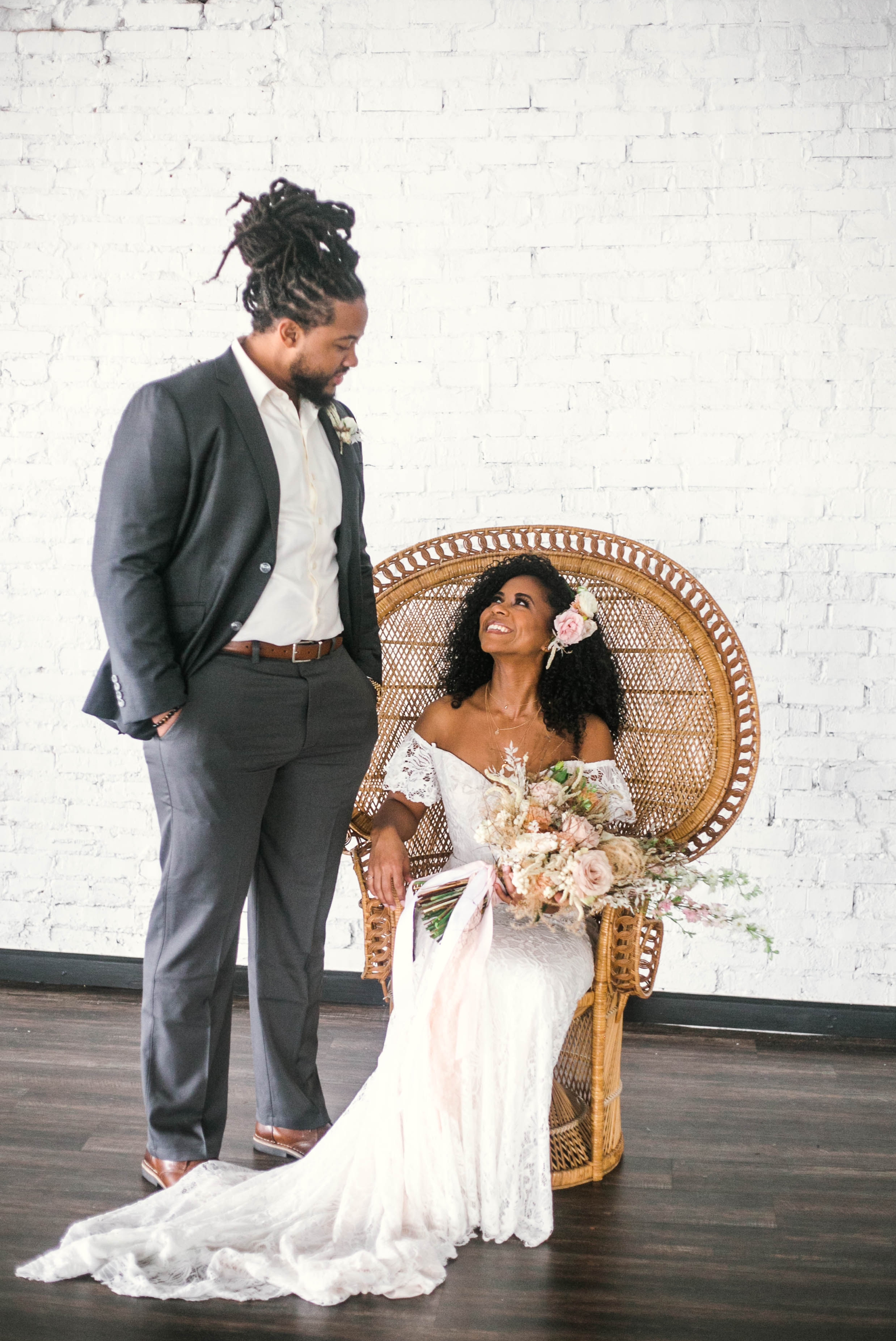  Indoor Bride and Groom Portraits, shot with natural light - black love - african american bride sitting in a Midcentury Woven Wicker Peacock Chair in a boho wedding dress with a big bouquet looking at her groom - honolulu, oahu, hawaii photographer 