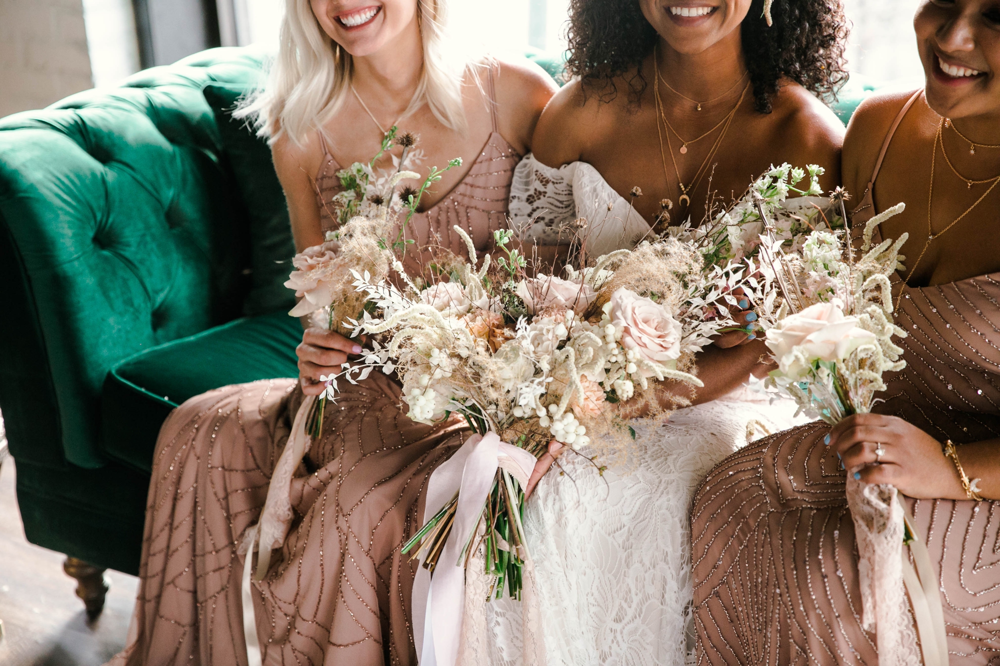  Indoor Natural light portrait of a black bride and her bridesmaids in a boho wedding dress with light pink bridesmaids dresses sitting on an emerald tufted sofa - laughing and having fun with each other- flowers in natural african american hair - oa