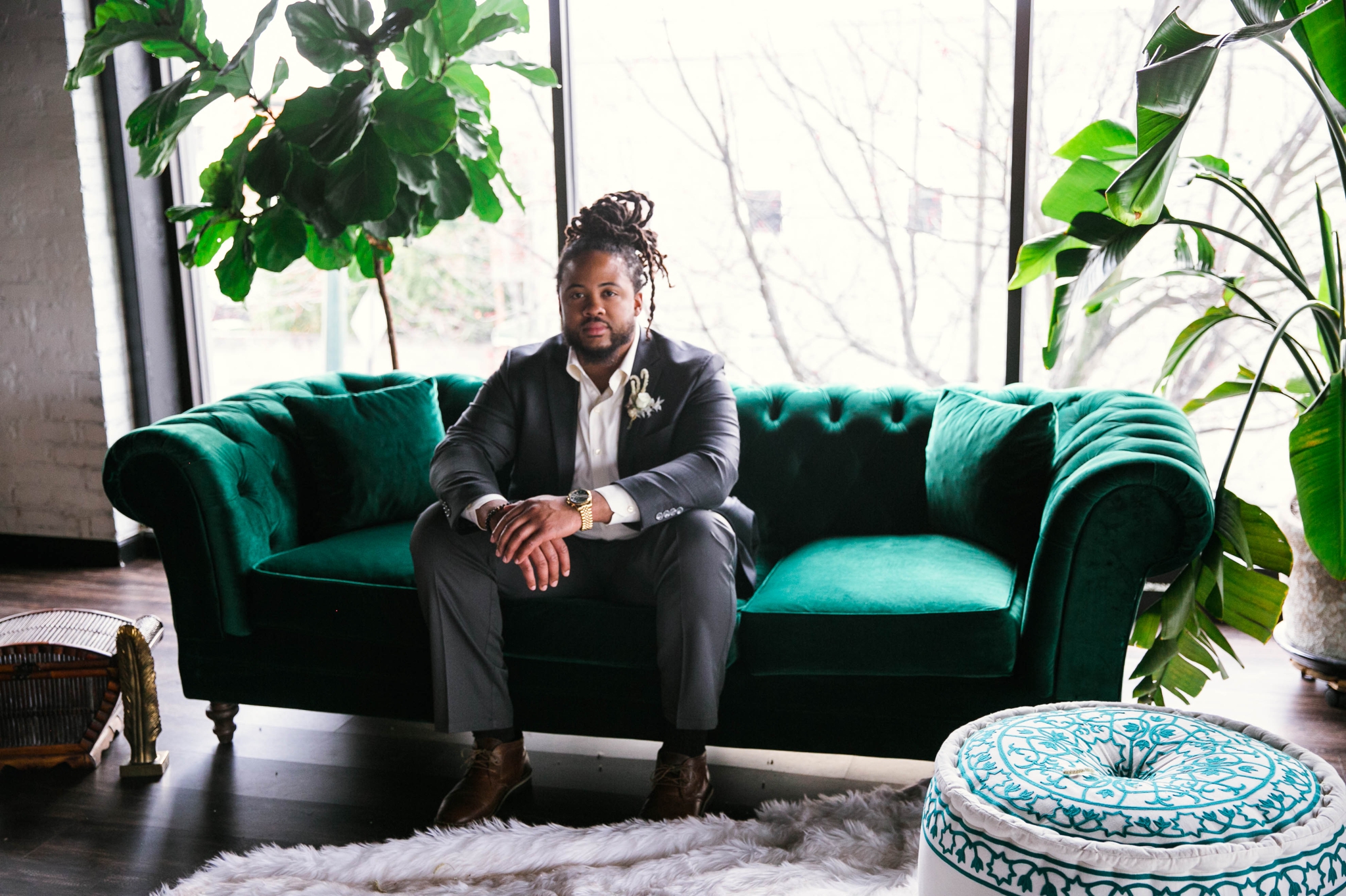  Indoor Natural light portrait of a black groom sitting on an emerald tufted sofa - laughing and having fun with each other- flowers in natural african american hair - oahu hawaii wedding photographer 
