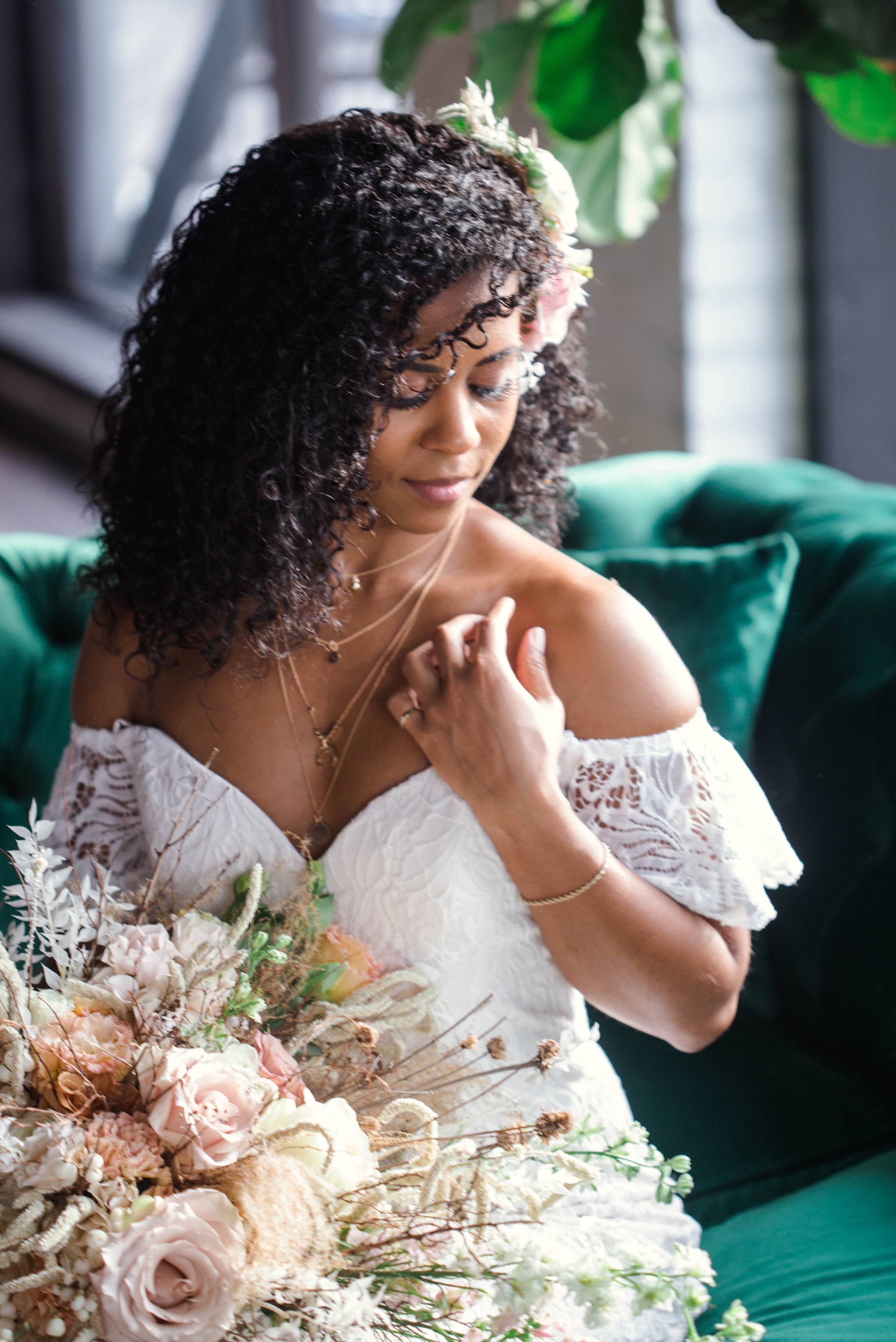 Indoor Natural light portrait of a black bride in a boho wedding dress sitting on an emerald tufted sofa - flowers in natural african american hair - oahu hawaii wedding photographer