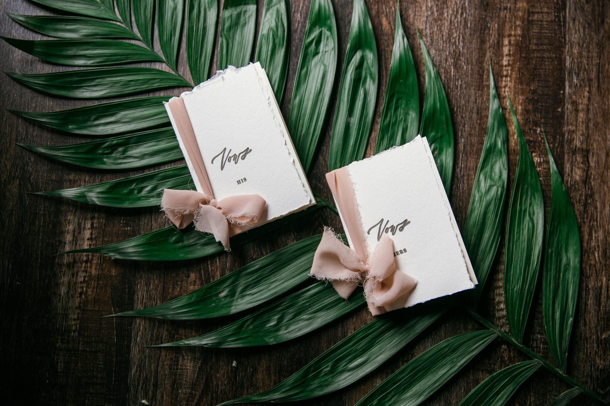  Lay flat of Wedding Vow books with a tropical leave as the background with light pink ribbon styled by Johanna Dye Photography designed by Tortoise.Design - Tropical Destination Wedding Inspiration - Oahu Hawaii Wedding Photographer 