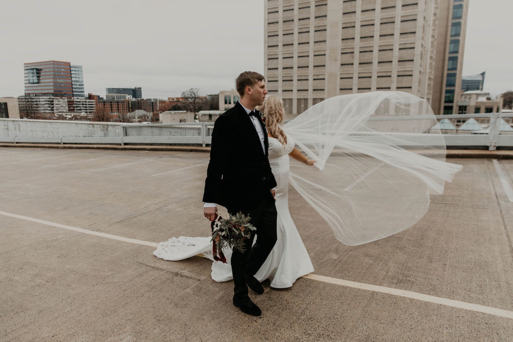 Downtown Bride and Groom portraits on top of a parking garage with the skyline in the background - Bride in an Allure Bridals Mermaid Gown - Burgundy Bridesmaids dresses by davids bridal Matt Smarsh and Johanna Dye - suites by the black tux - Raleigh North Carolina Urban Edgy Downtown Wedding - suits by the black tux