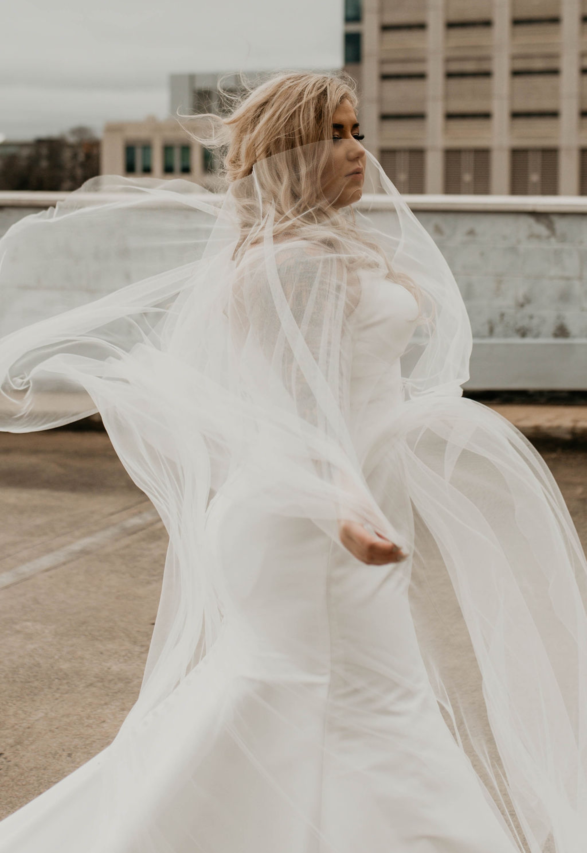 Downtown Bride portraits on top of a parking garage with the skyline in the background - Bride playing with her noontothemoon bridal cape - Bride in an Allure Bridals Mermaid Gown - Burgundy Bridesmaids dresses by davids bridal Matt Smarsh and Johanna Dye - suites by the black tux - Raleigh North Carolina Urban Edgy Downtown Wedding - suits by the black tux