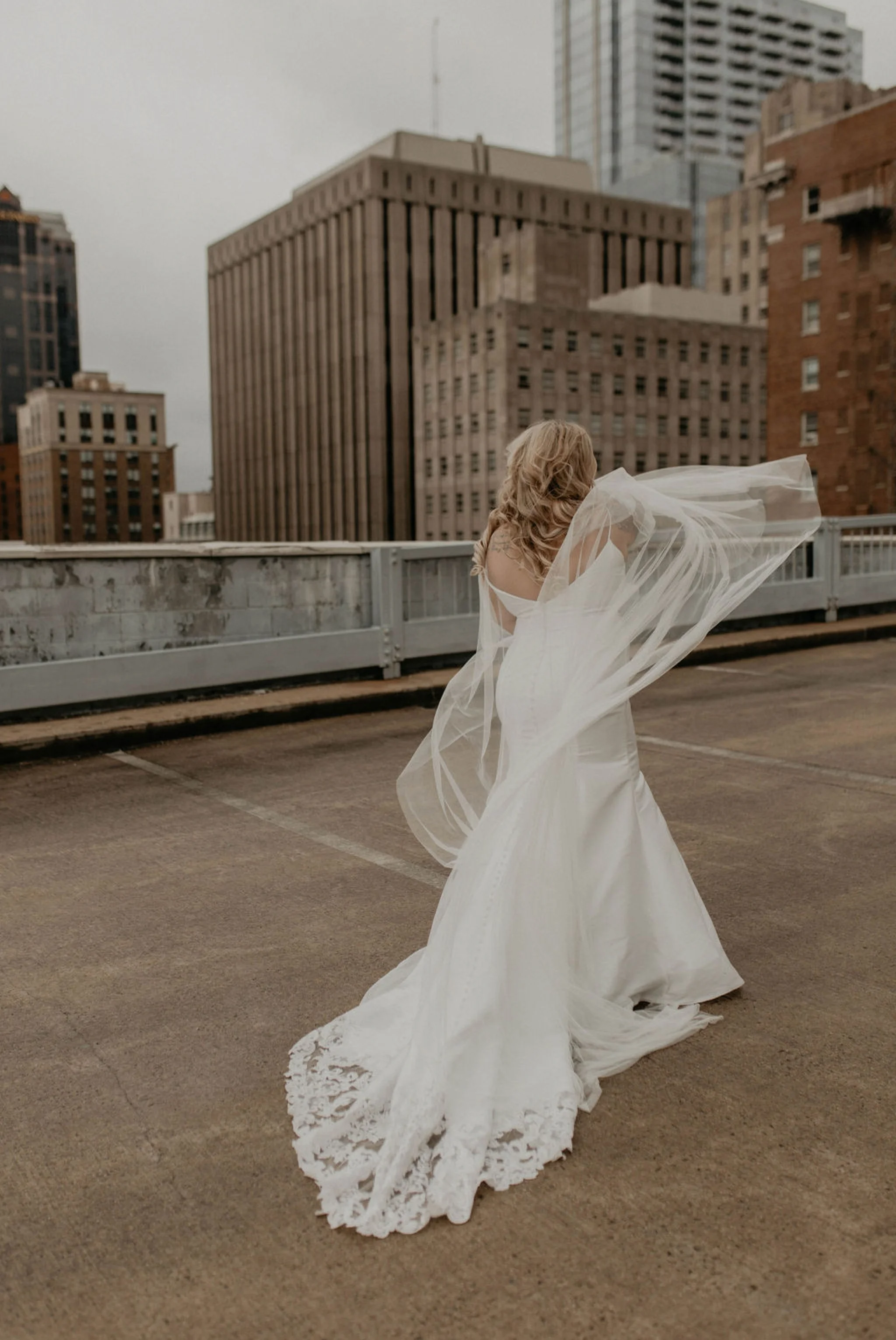 Downtown Bride portraits on top of a parking garage with the skyline in the background - Bride playing with her noontothemoon bridal cape - Bride in an Allure Bridals Mermaid Gown - Burgundy Bridesmaids dresses by davids bridal Matt Smarsh and Johanna Dye - suites by the black tux - Raleigh North Carolina Urban Edgy Downtown Wedding - suits by the black tux