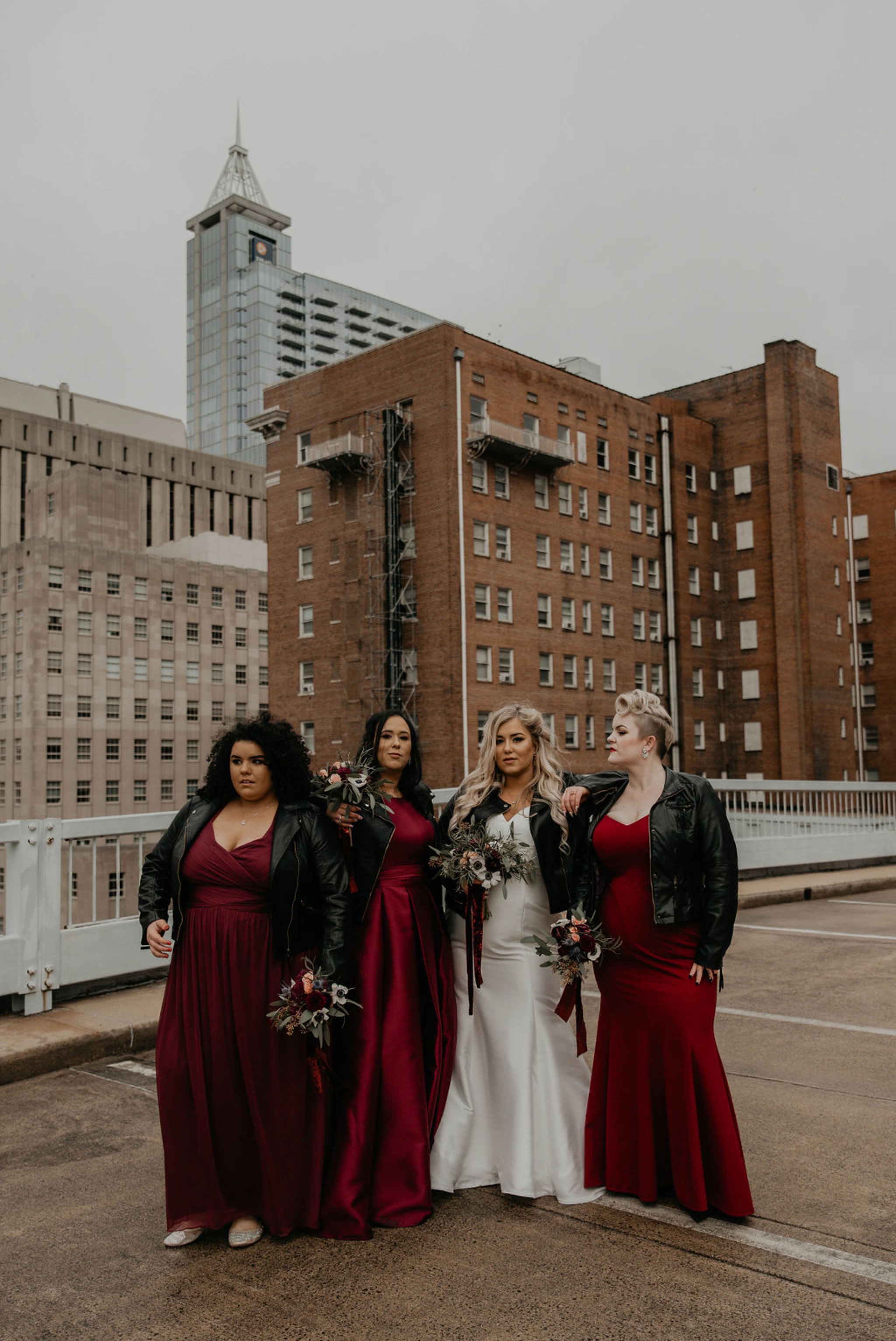 Edgy Bridesmaids portraits with Leather Jackets downtown with the skyline in the background - Bride in an Allure Bridals Mermaid Gown - Burgundy Bridesmaids dresses by davids bridal Matt Smarsh and Johanna Dye - suites by the black tux - Raleigh North Carolina Urban Downtown Wedding - suits by the black tux