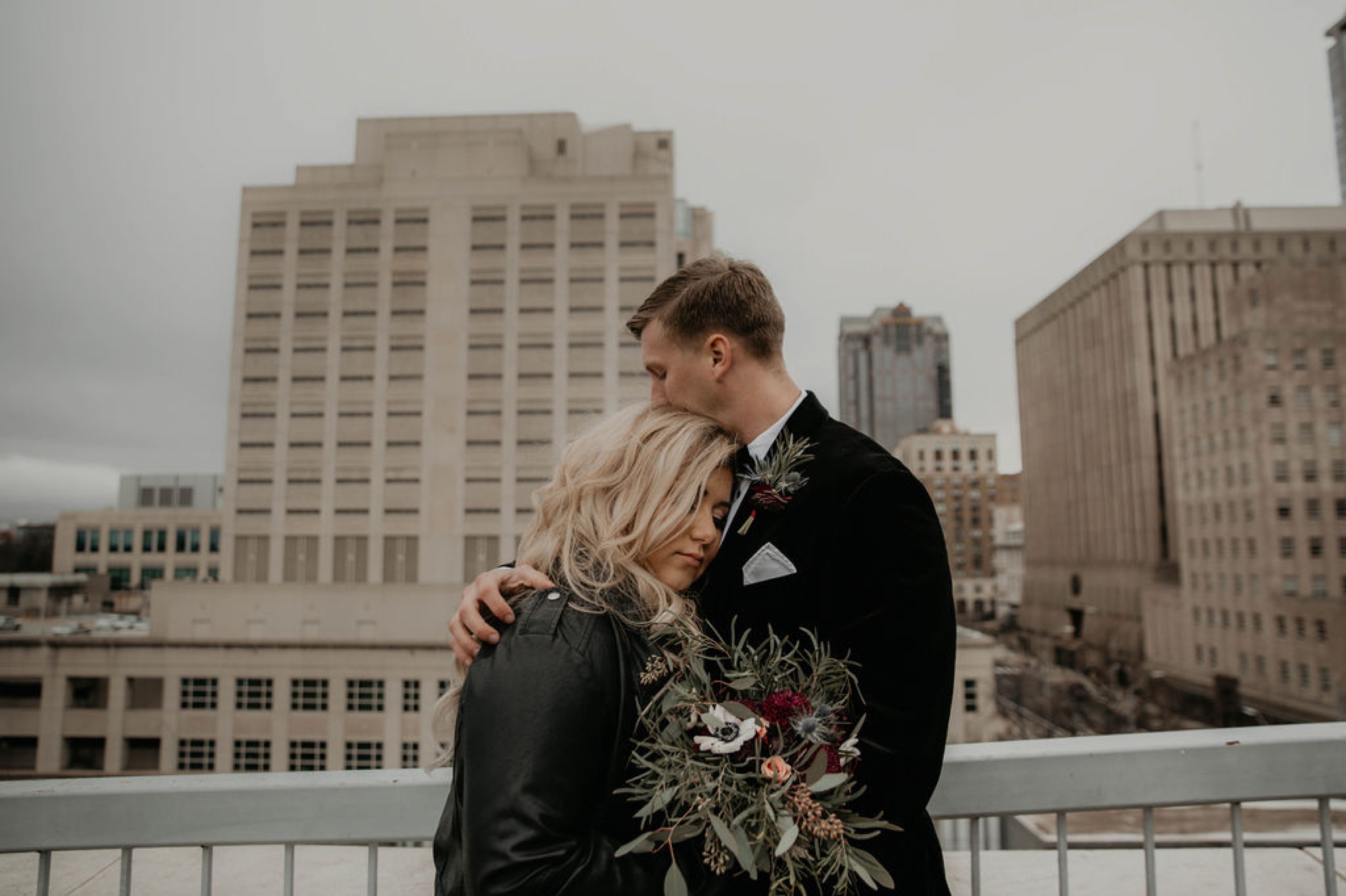 Wedding Portraits - Groom hugging bride - Bride in an Allure Bridals Mermaid Gown and a leather jacket - Burgundy Bridesmaids dresses by davids bridal Matt Smarsh and Johanna Dye - suites by the black tux - Raleigh North Carolina Urban Downtown Wedding - suits by the black tux