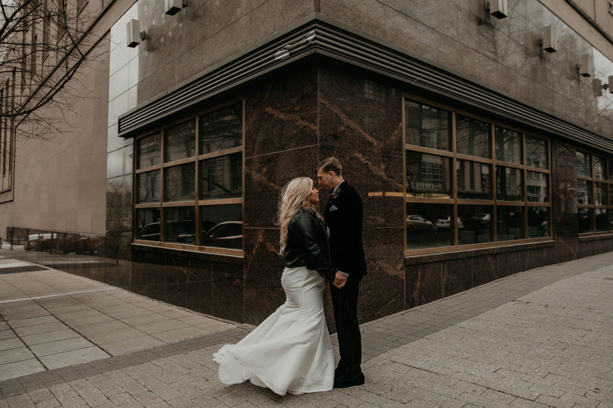 bride and groom looking at each other in downtown raleigh - Bride in an Allure Bridals Mermaid Gown and a leather jacket - Burgundy Bridesmaids dresses by davids bridal Matt Smarsh and Johanna Dye - suites by the black tux - Raleigh North Carolina Urban Downtown Wedding - suits by the black tux