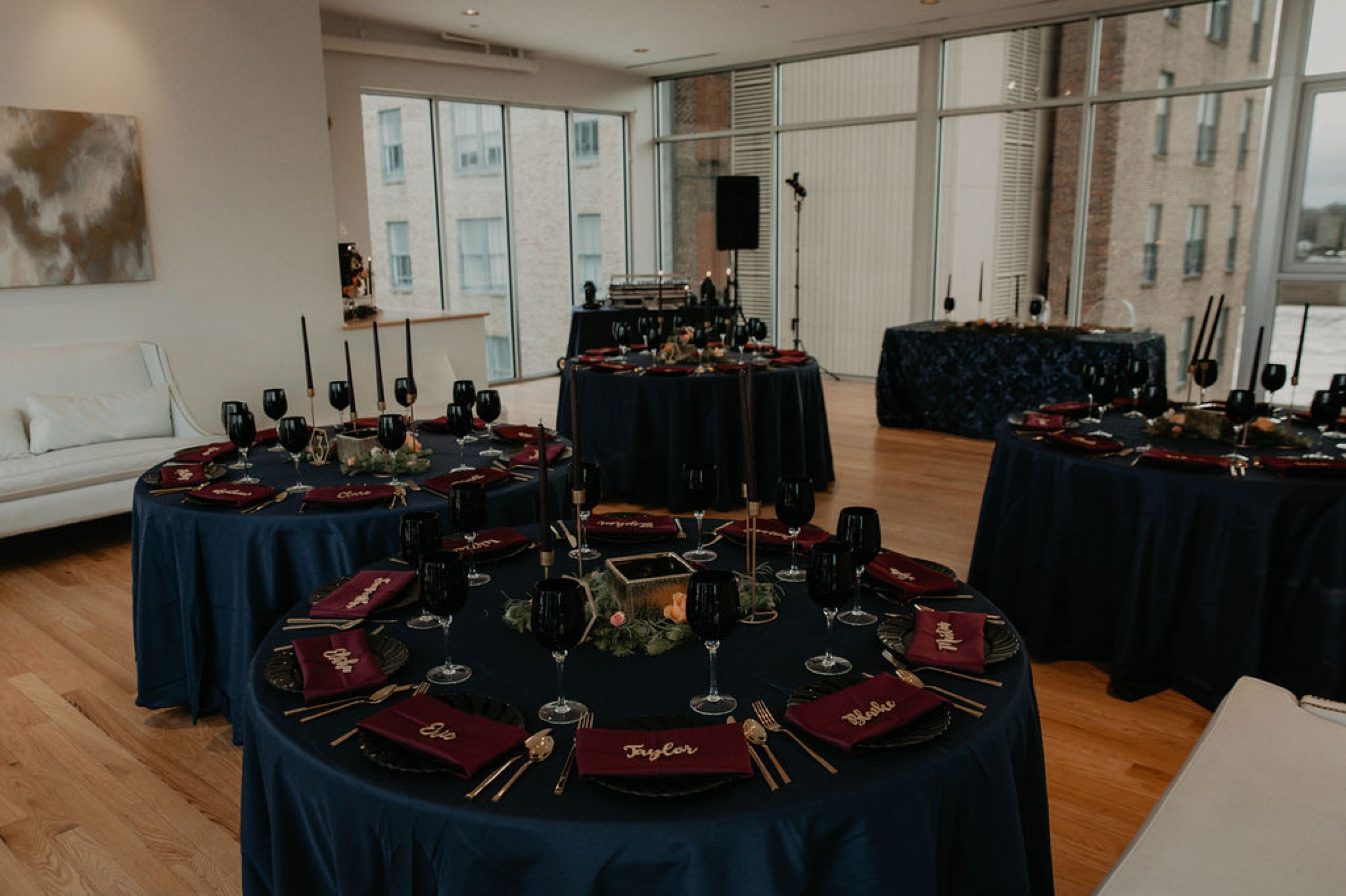 sweetheart table - dark wedding table decorations - Navy tablecloth with burgundy napkins and gold laser cut name place cards, gold silverwear and black plates and black wine glasses by ce rental - dark flowers centerpiece - gold table number - gold candle stick holder with black candles - Matt Smarsh and Johanna Dye - Raleigh North Carolina Urban Downtown Wedding at the Glass Box at 230