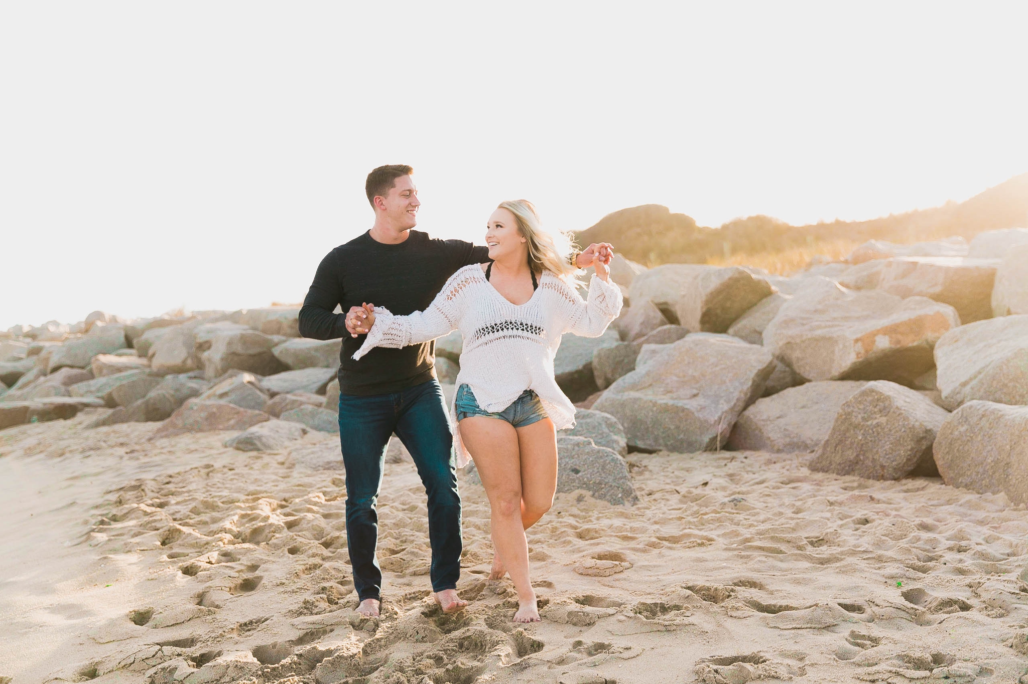  couple being playful at the beach and doing the titanic flying pose at sunset during golden hour light - girl wearing ripped jeans shorts and a white free people sweater - Casual Beach Engagement Photography Session - Honolulu Oahu Hawaii Wedding Ph