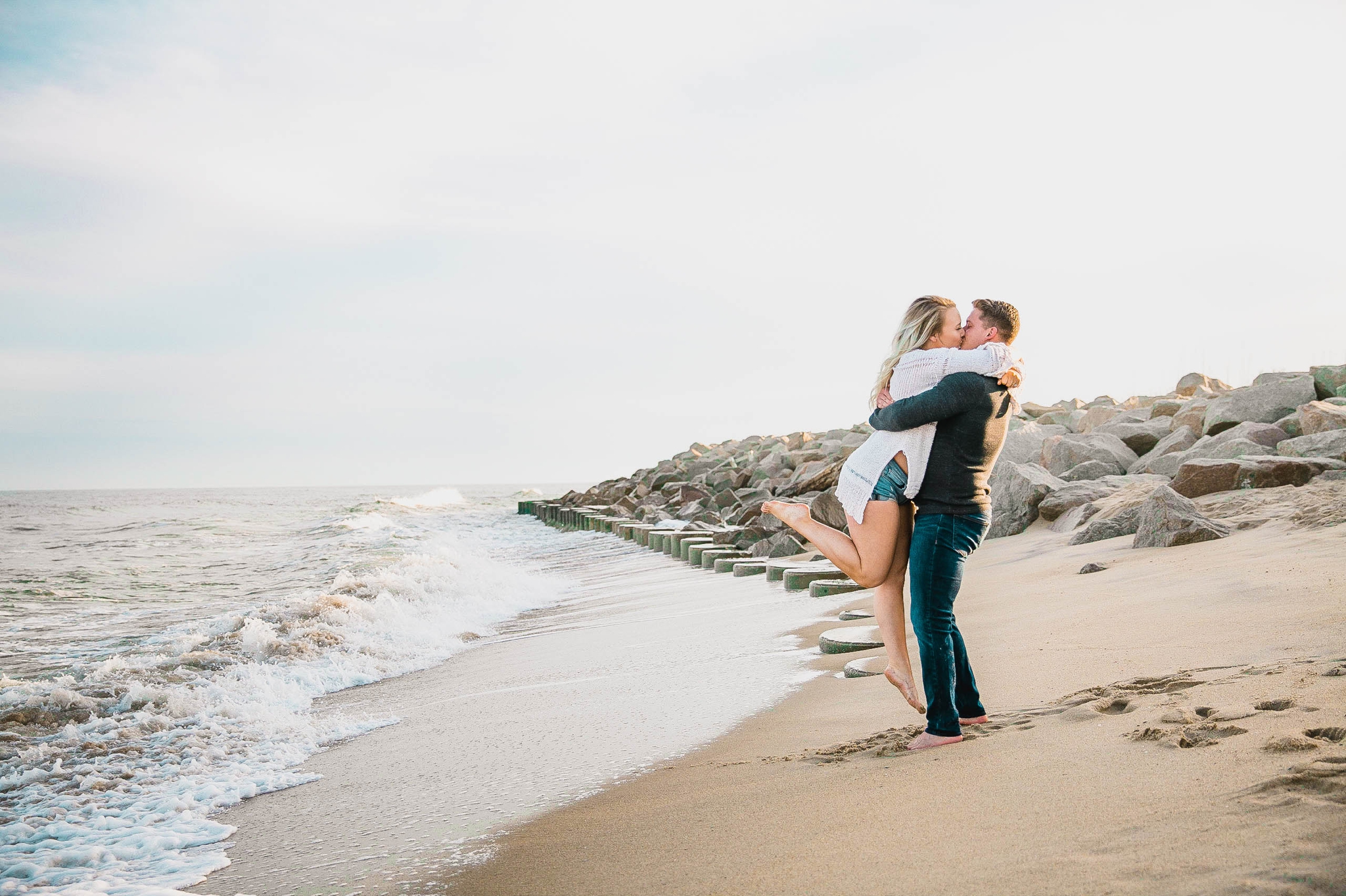  guy picking up his fiance on the beach for a kiss - girl wearing ripped jeans shorts and a white free people sweater - Casual Beach Engagement Photography Session - Honolulu Oahu Hawaii Wedding Photographer - Johanna Dye 