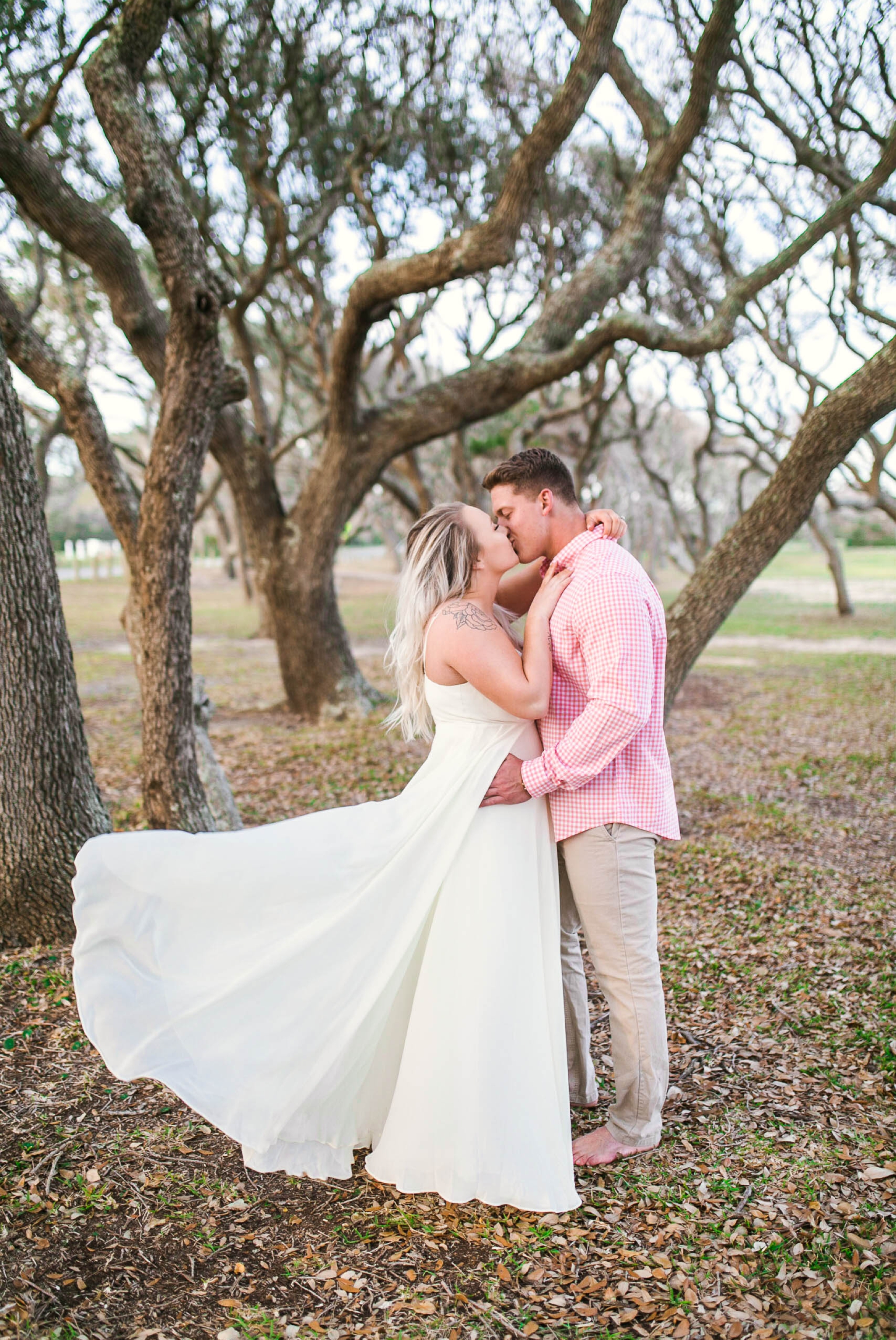  Engagement Photography Session beneath tropical trees - man kissing his fiance - girl is wearing a white flowy maxi dress from lulus - Honolulu Oahu Hawaii Wedding Photographer - Johanna Dye 