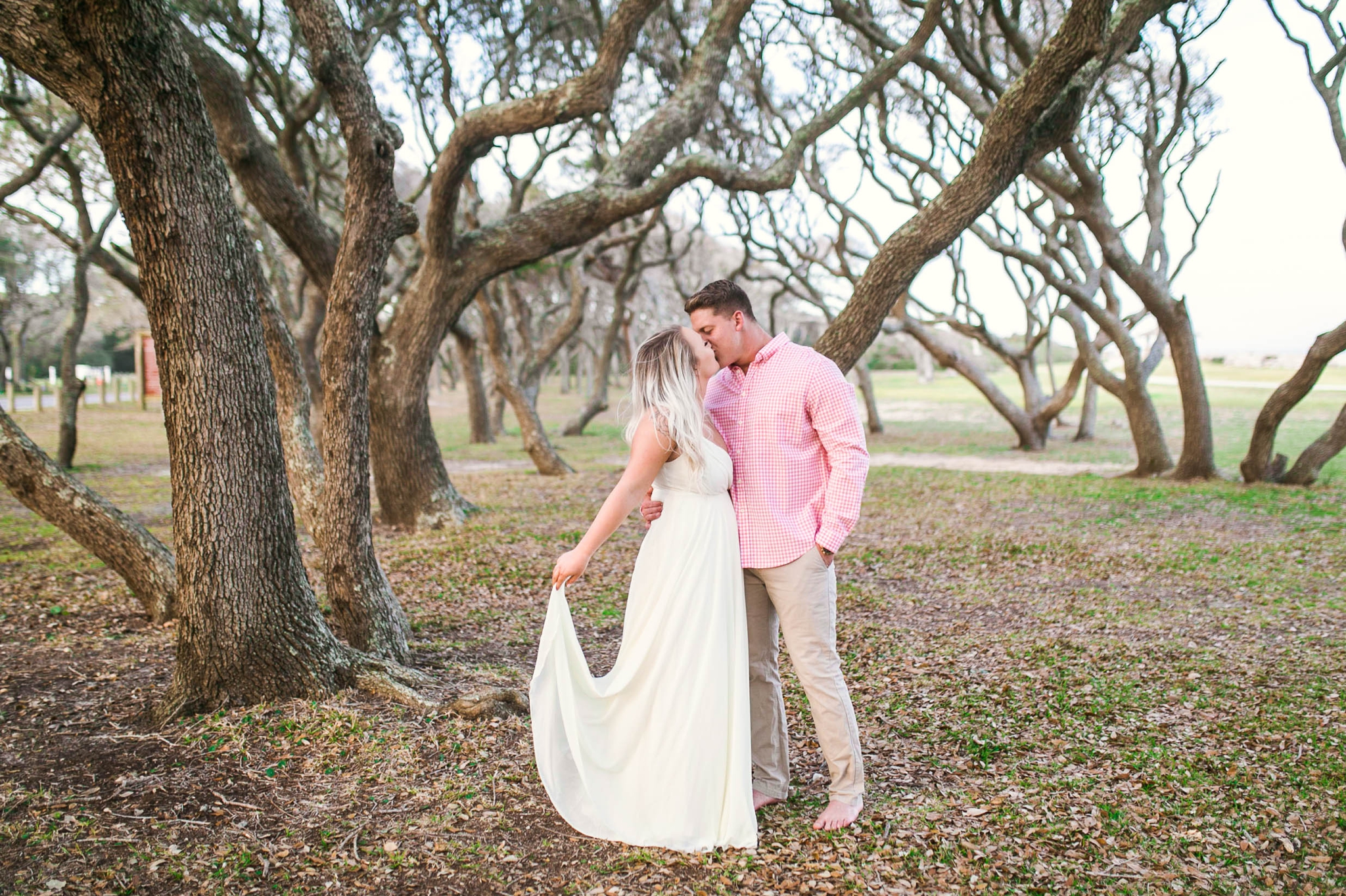  Engagement Photography Session beneath tropical trees - man kissing his fiance - girl is wearing a white flowy maxi dress from lulus that she is playing with  - Honolulu Oahu Hawaii Wedding Photographer - Johanna Dye 