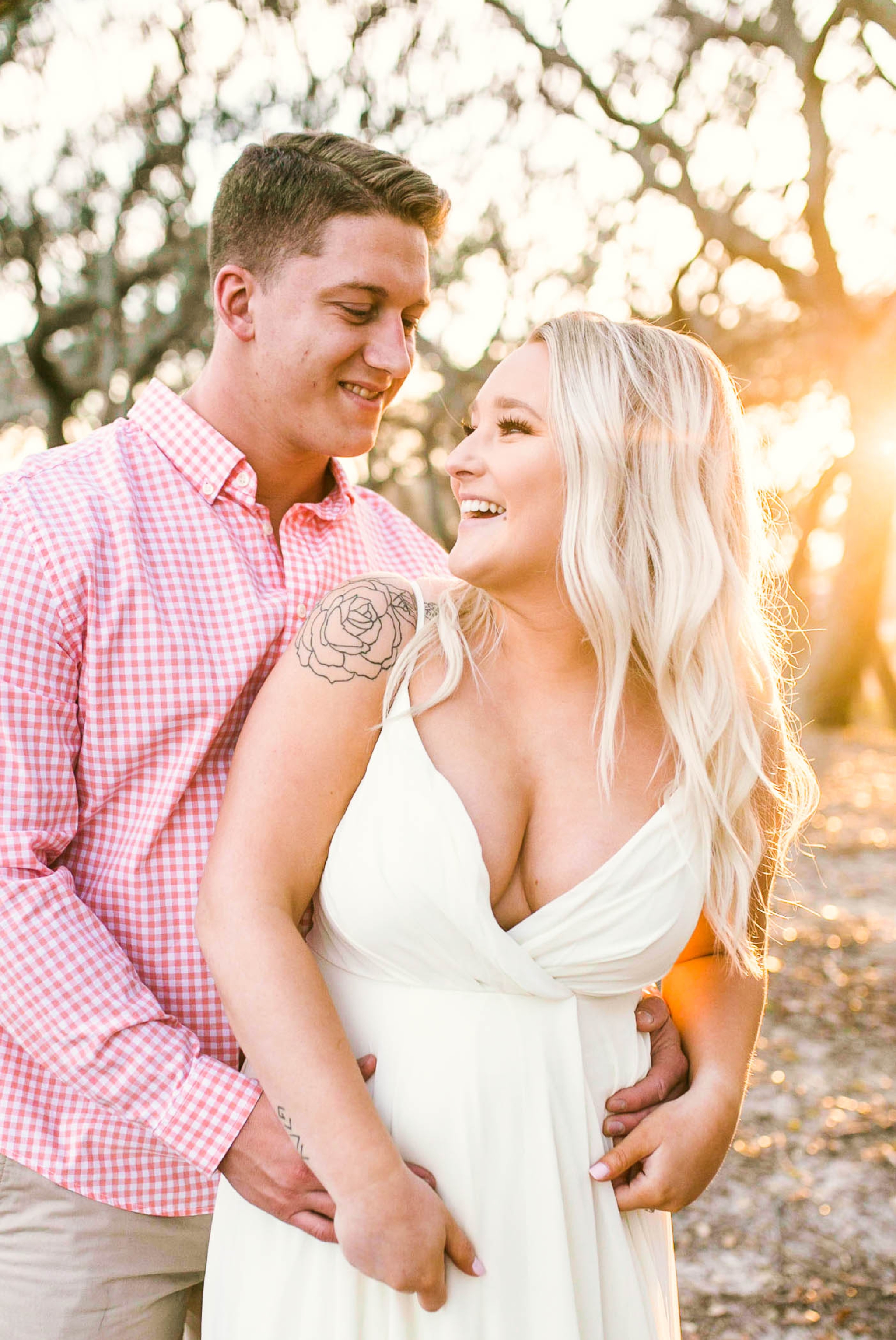  Engagement Photography Session beneath tropical trees at sunset during golden hour light - couple is laughing at each other - girl is wearing a white flowy maxi dress from lulus - Honolulu Oahu Hawaii Wedding Photographer - Johanna Dye 