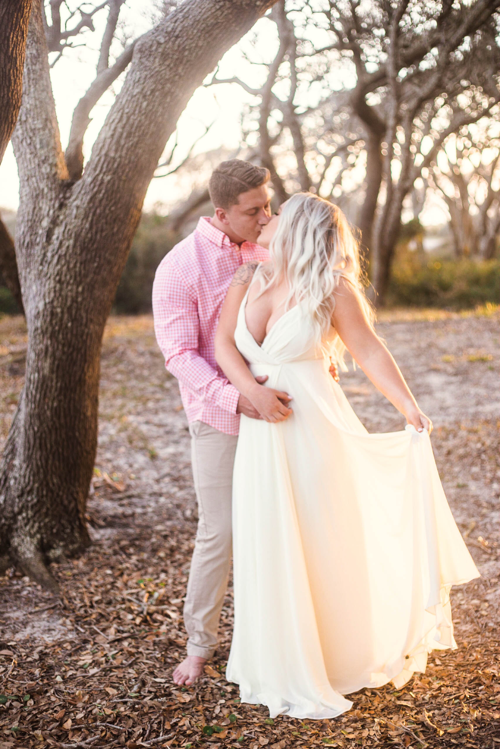  Engagement Photography Session beneath tropical trees at sunset during golden hour light - man kissing his fiance - girl is wearing a white flowy maxi dress from lulus - Honolulu Oahu Hawaii Wedding Photographer - Johanna Dye 