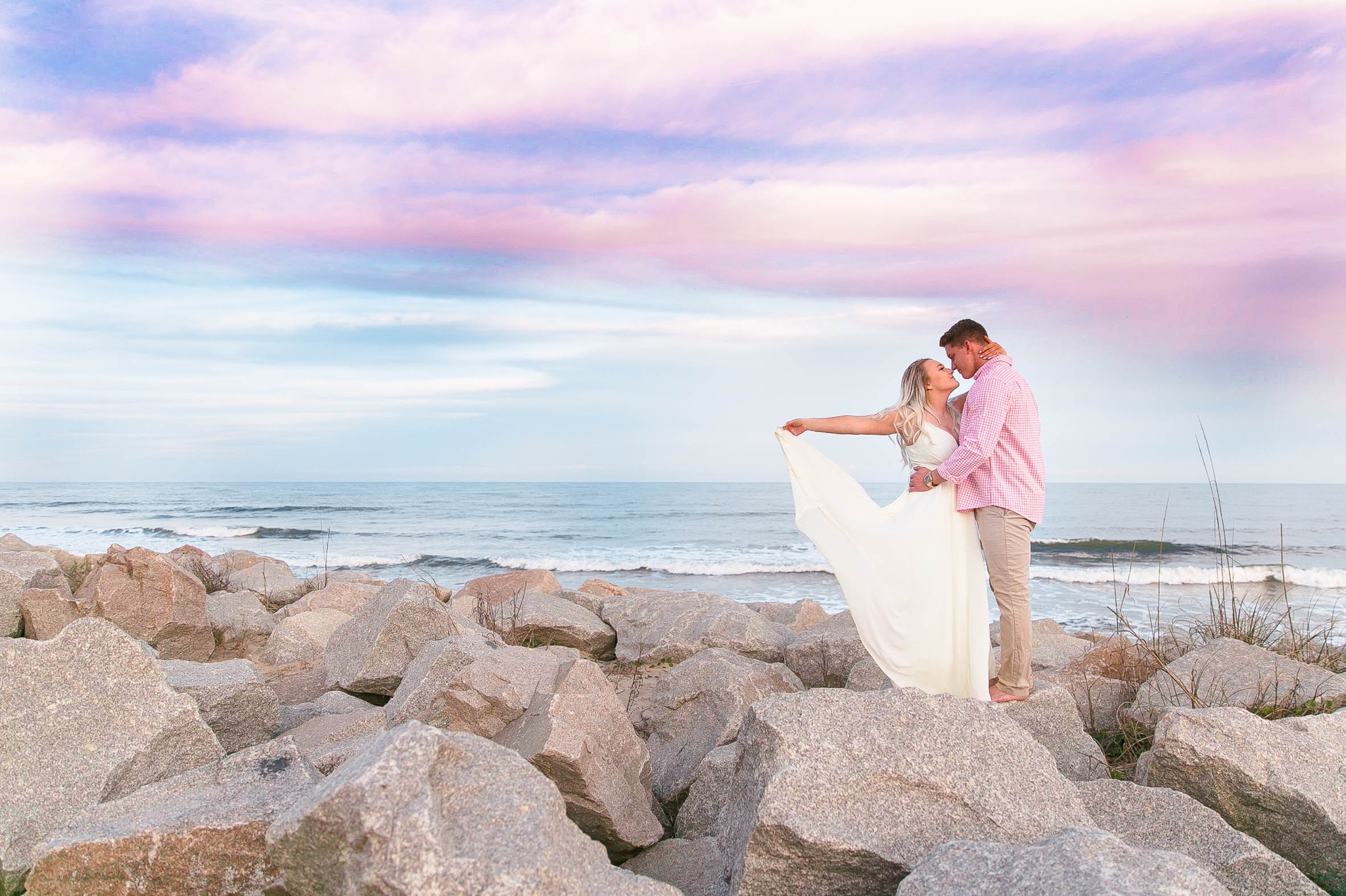  Engagement Photography Session at the beach on top of rocks with a cotton candy sky in the background - couple is kissing  - girl is wearing a white flowy maxi dress from lulus - Honolulu Oahu Hawaii Wedding Photographer - Johanna Dye 