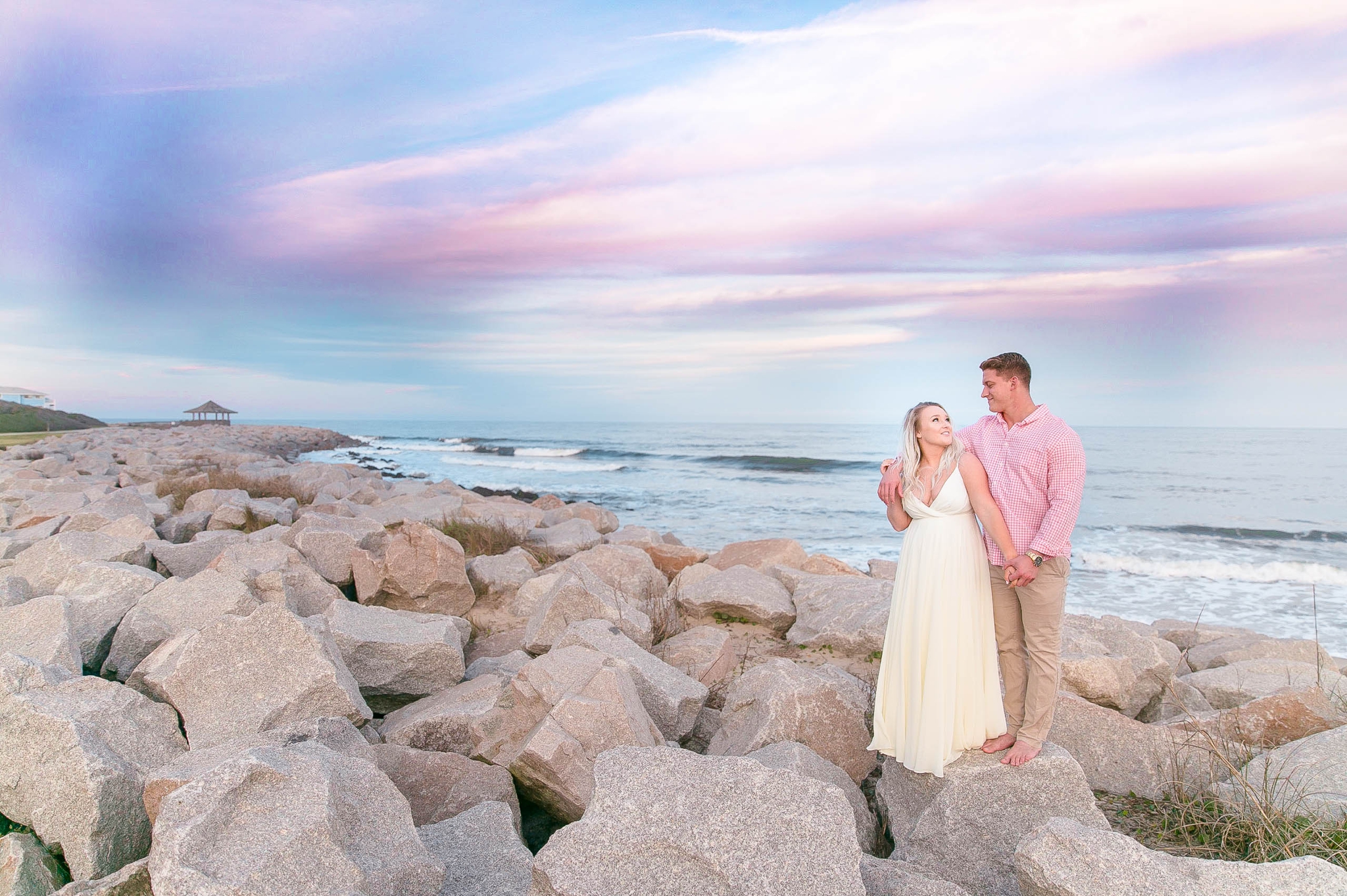  Engagement Photography Session at the beach on top of rocks with a cotton candy sky in the background - couple is standing up - girl is wearing a white flowy maxi dress from lulus - Honolulu Oahu Hawaii Wedding Photographer - Johanna Dye 