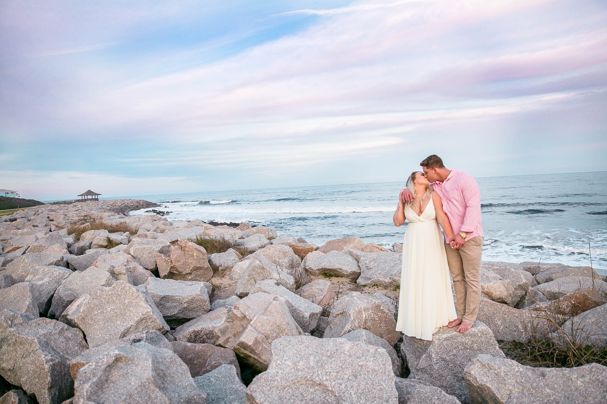  Engagement Photography Session at the beach on top of rocks with a cotton candy sky in the background - couple is hugging each other- girl is wearing a white flowy maxi dress from lulus - Honolulu Oahu Hawaii Wedding Photographer - Johanna Dye 