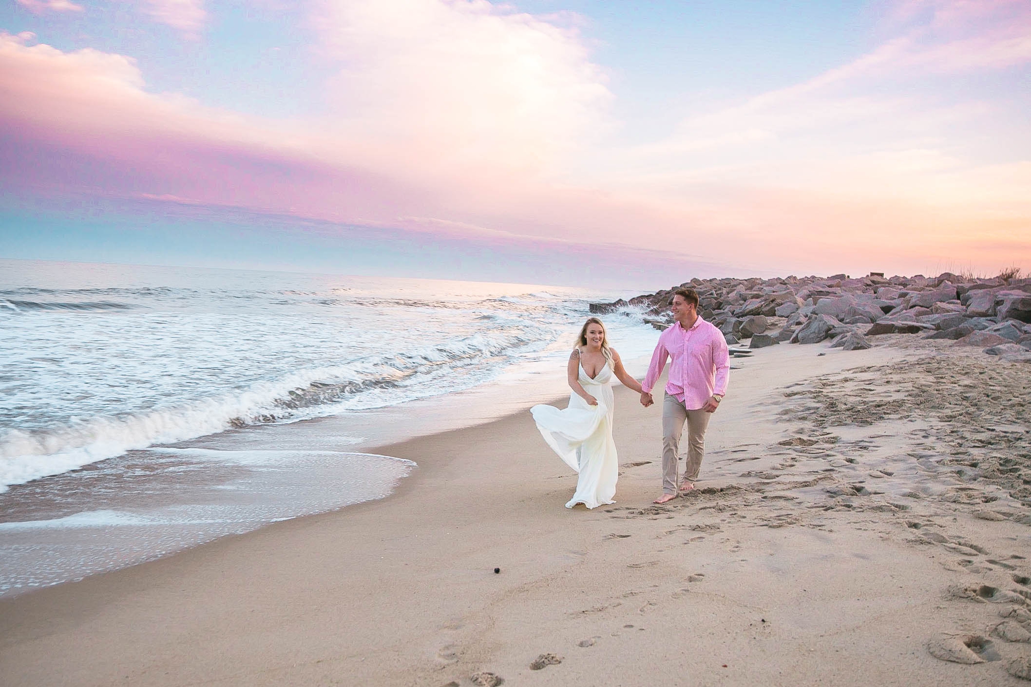  Romantic Engagement Photography Session at the beach during sunset with a cotton candy sky - couple is walking in the sand - girl is wearing a white flowy maxi dress from lulus - Honolulu Oahu Hawaii Wedding Photographer - Johanna Dye 