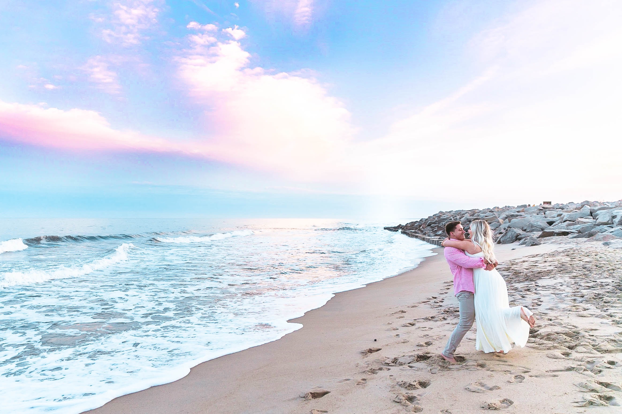  Romantic Engagement Photography Session at the beach during sunset with a cotton candy sky - guy is picking up his fiance for a kiss and swinging her around - girl is wearing a white flowy maxi dress from lulus - Honolulu Oahu Hawaii Wedding Photogr