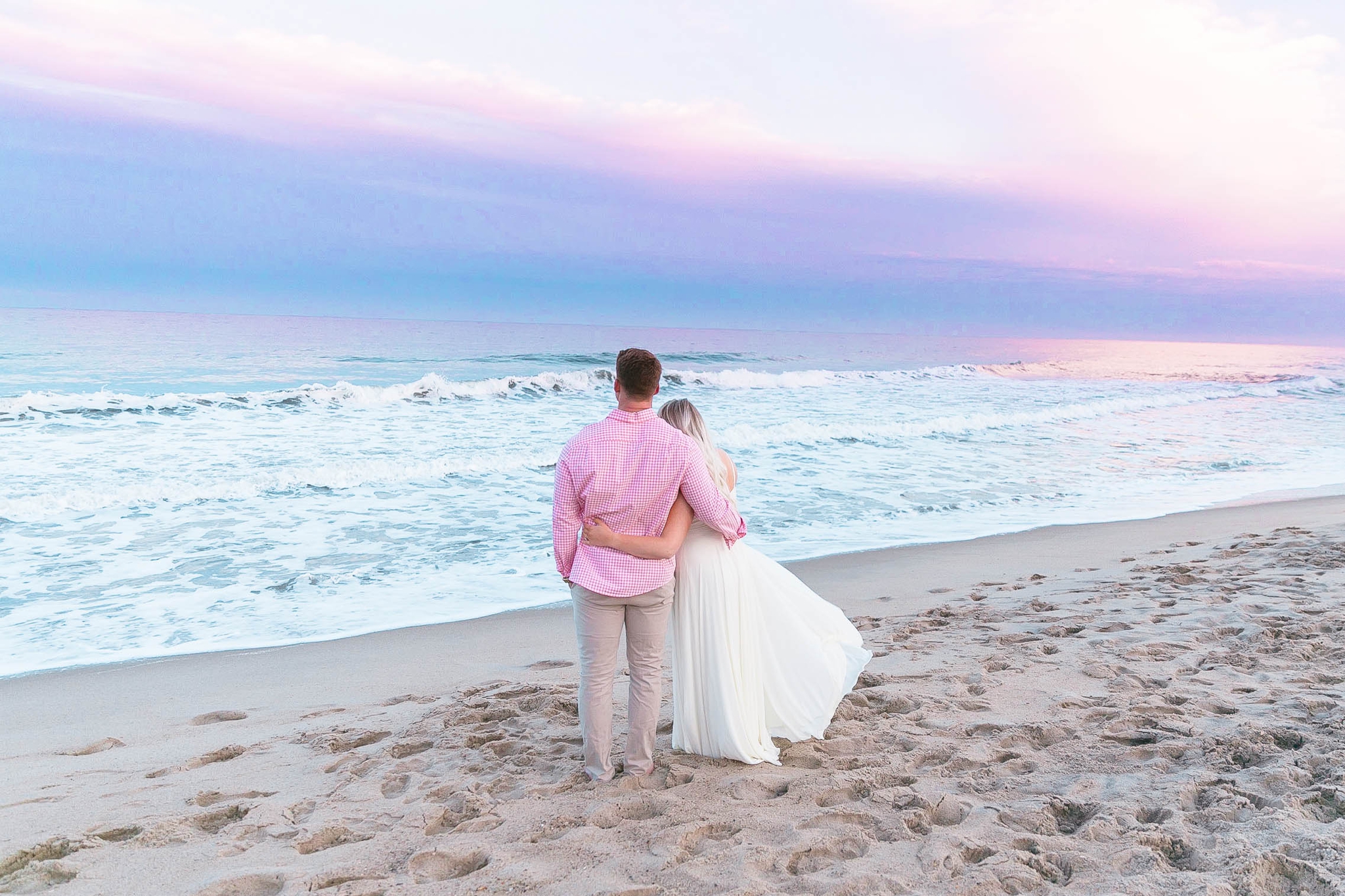  Romantic Engagement Photography Session at the beach during sunset with a cotton candy sky - couple is looking at the ocean while standing in the sand - girl is wearing a white flowy maxi dress from lulus - Honolulu Oahu Hawaii Wedding Photographer 