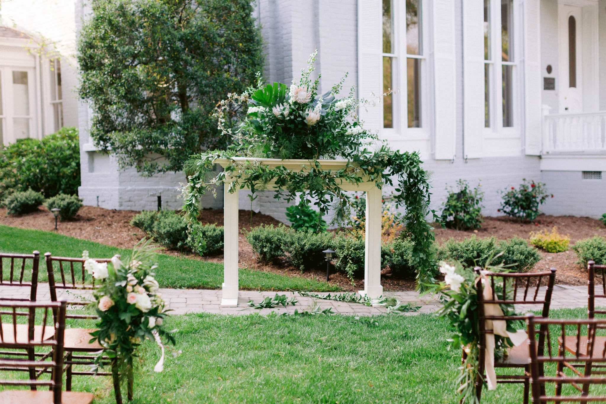  Garden Outdoor Ceremony with brown wooden chairs in front of an all white  mansion - Wedding  Fireplace mantel with lush green decorations - Honolulu, Oahu, Hawaii Wedding Photographer - Johanna Dye Photography 