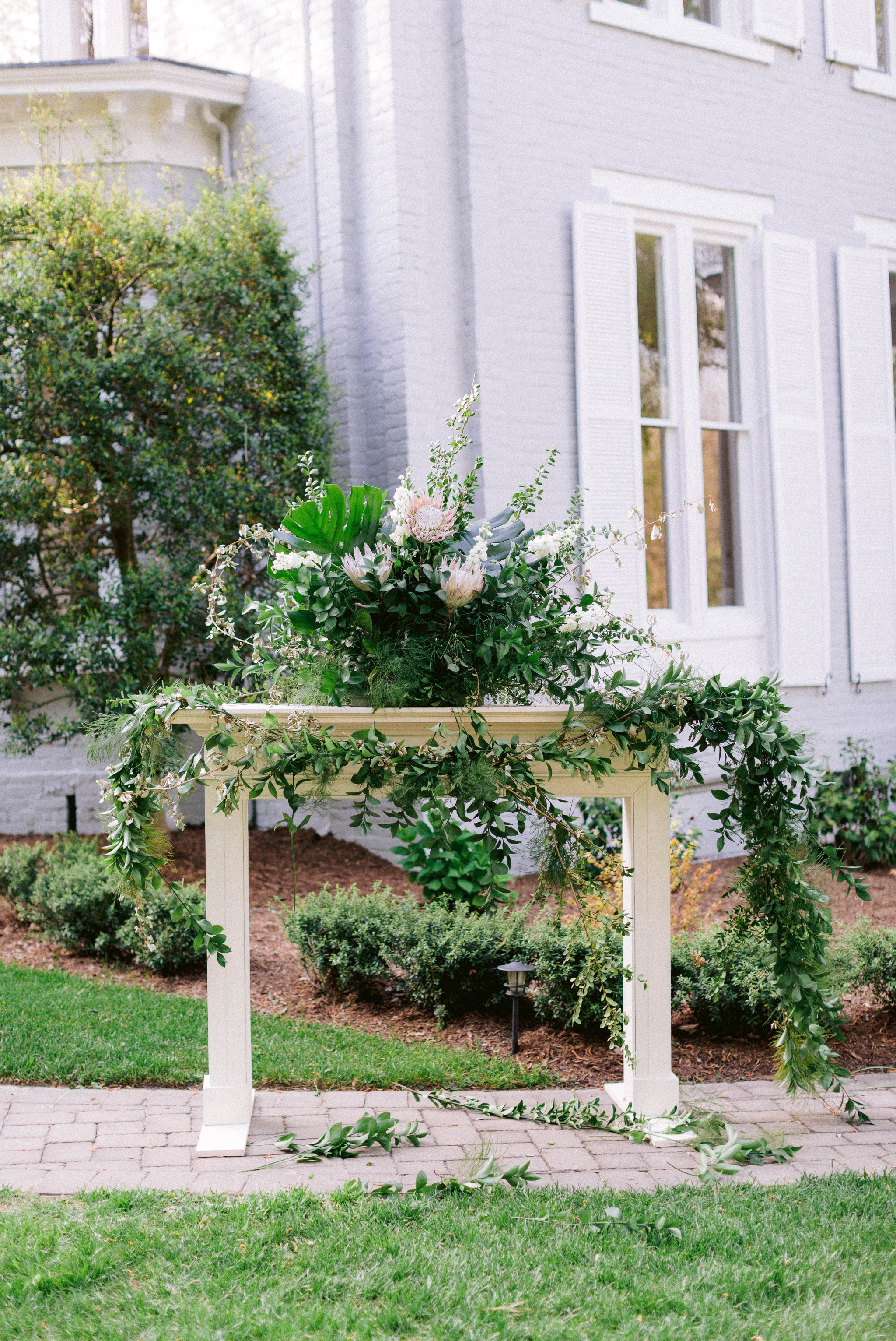  Garden Outdoor Ceremony with brown wooden chairs in front of an all white mansion - Wedding Fireplace mantel with lush green decorations - Honolulu, Oahu, Hawaii Wedding Photographer - Johanna Dye Photography 