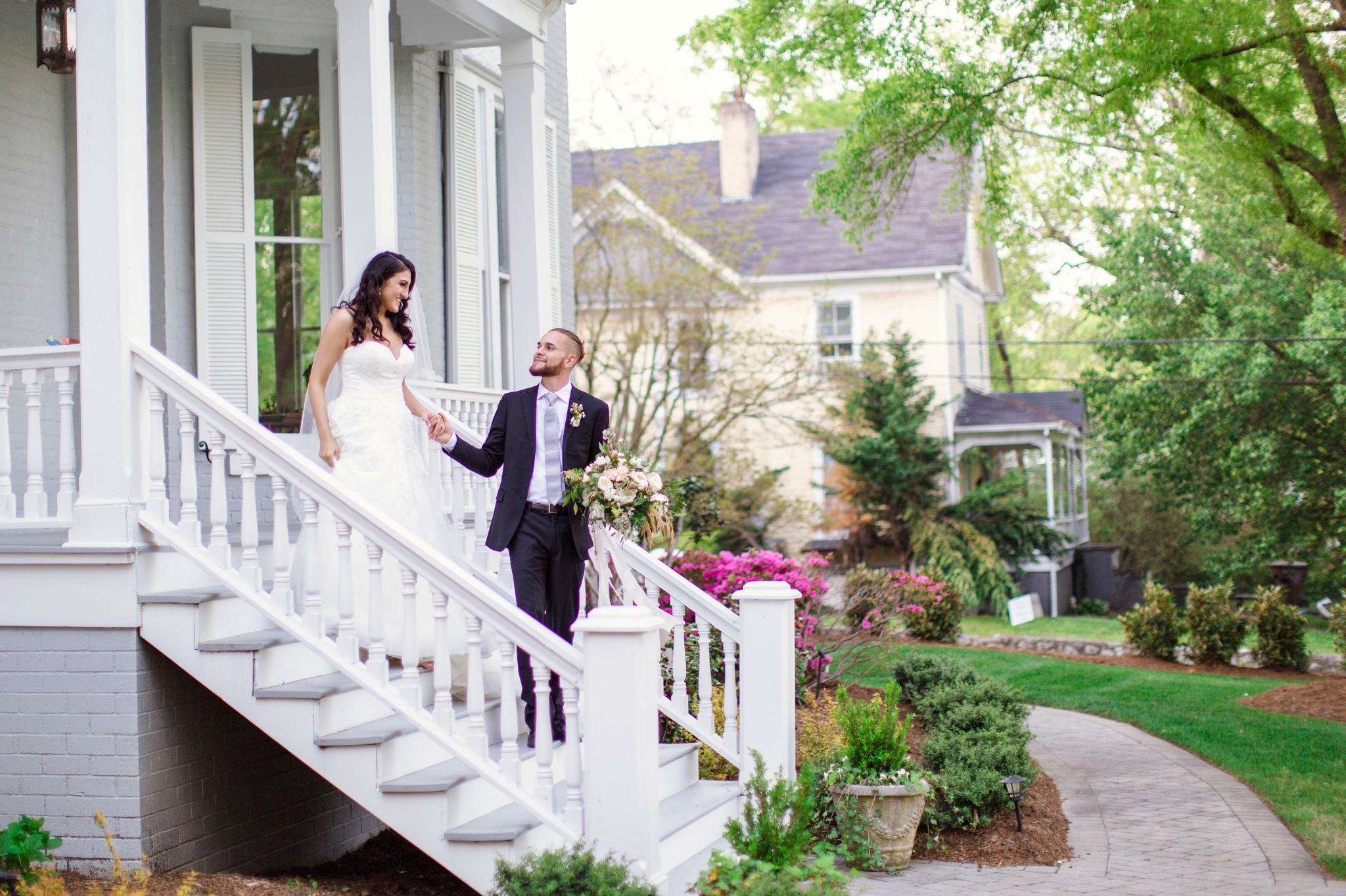  Groom leading his bride down the front steps -Couple Kissing - Wedding Portraits on the front porch of an all white luxury estate mansion - Bride is wearing a Aline Ballgown by Cherish by Southern Bride with a long cathedral veil - Groom is wearing 