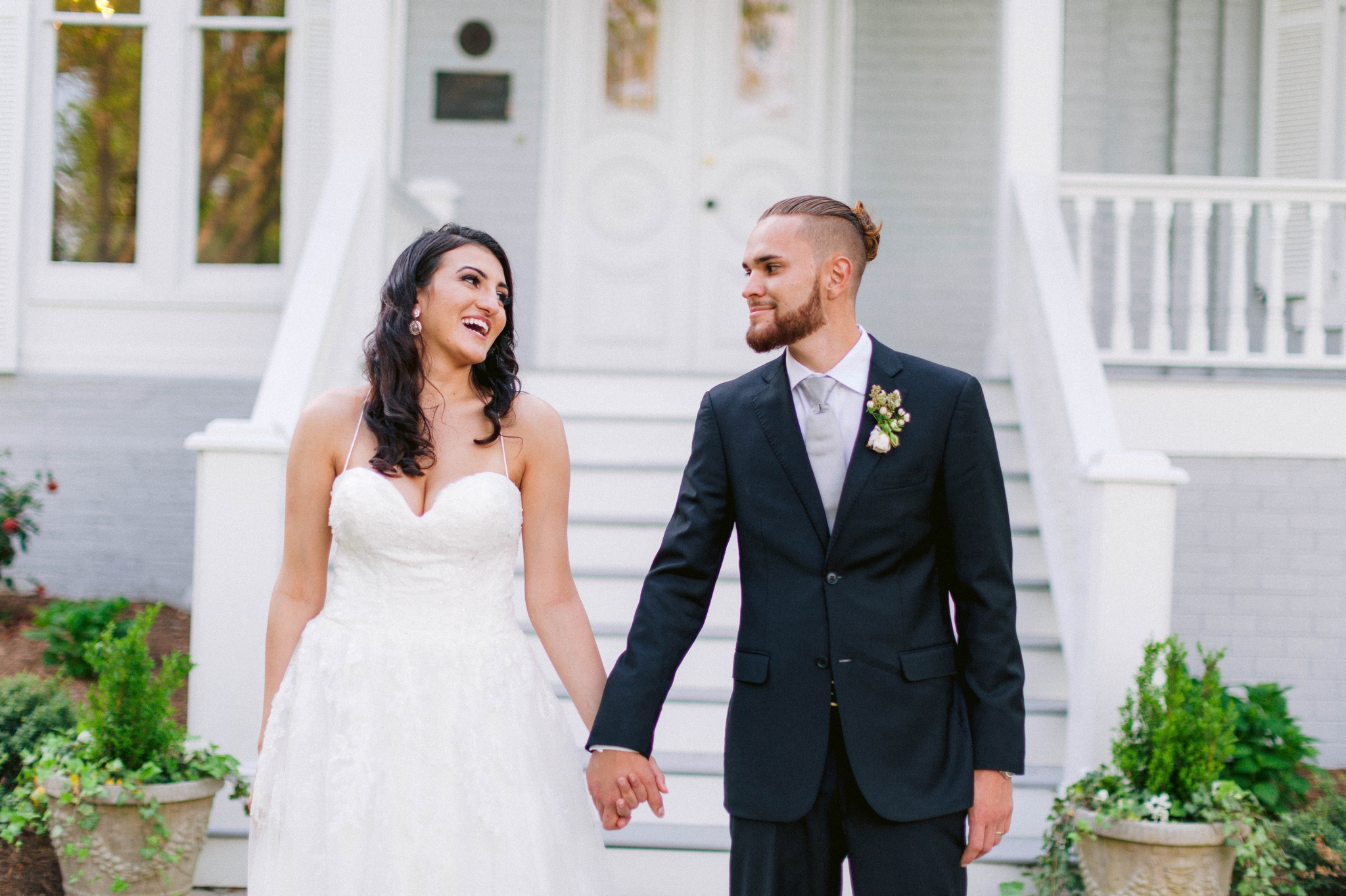  Couple looking at each other - Wedding Portraits on the front porch of an all white luxury estate - Bride is wearing a Aline Ballgown by Cherish by Southern Bride with a long cathedral veil - Groom is wearing a black suit by Generation Tux and has a