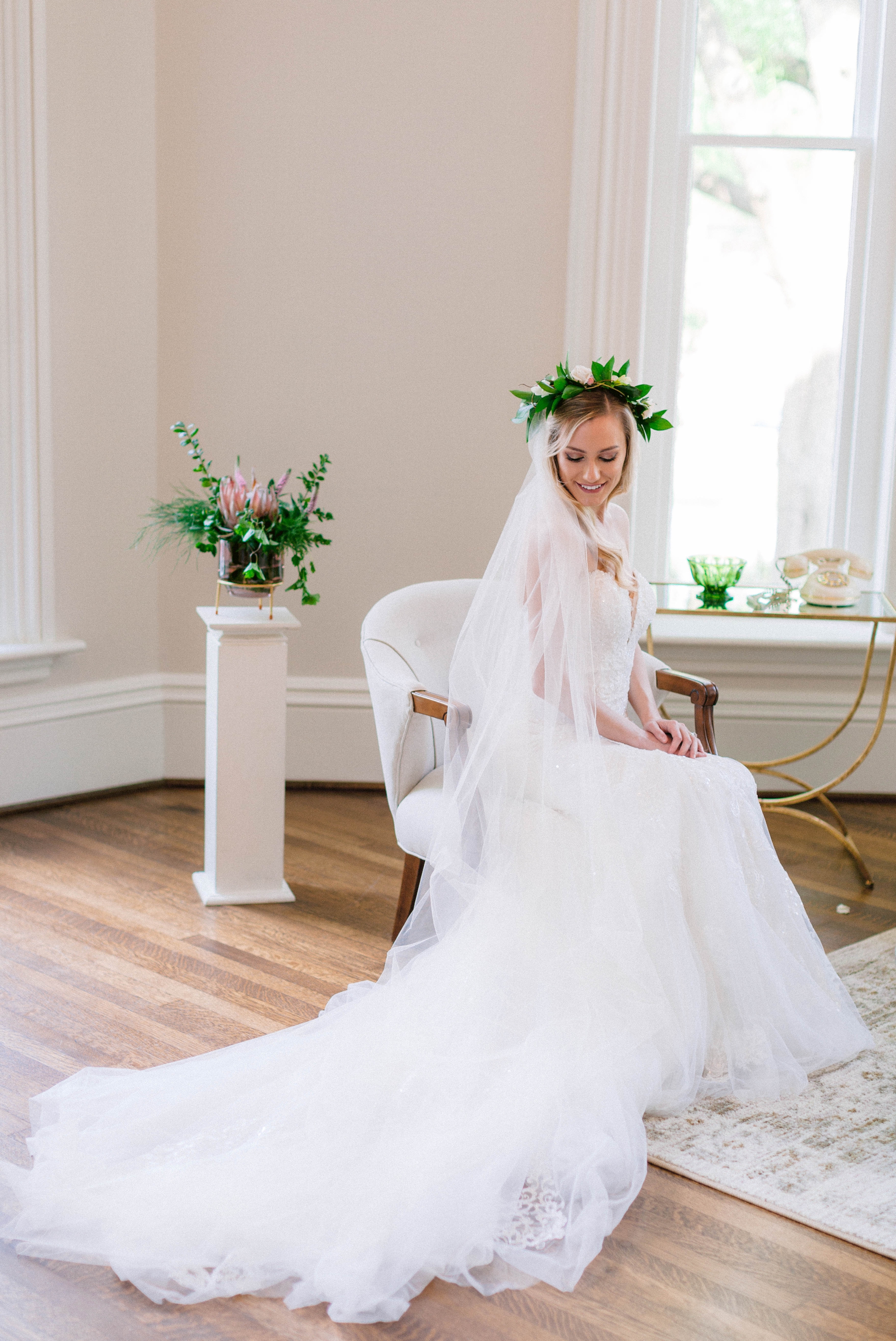  Indoor Bridal Portraits in an all white room at a luxury estate with natural light before the ceremony - Bride is wearing a Hawaiian Flower Crown and a cathedral veil in a Wedding Gown by Stella York and sitting in a chair  - Honolulu Oahu Hawaii We