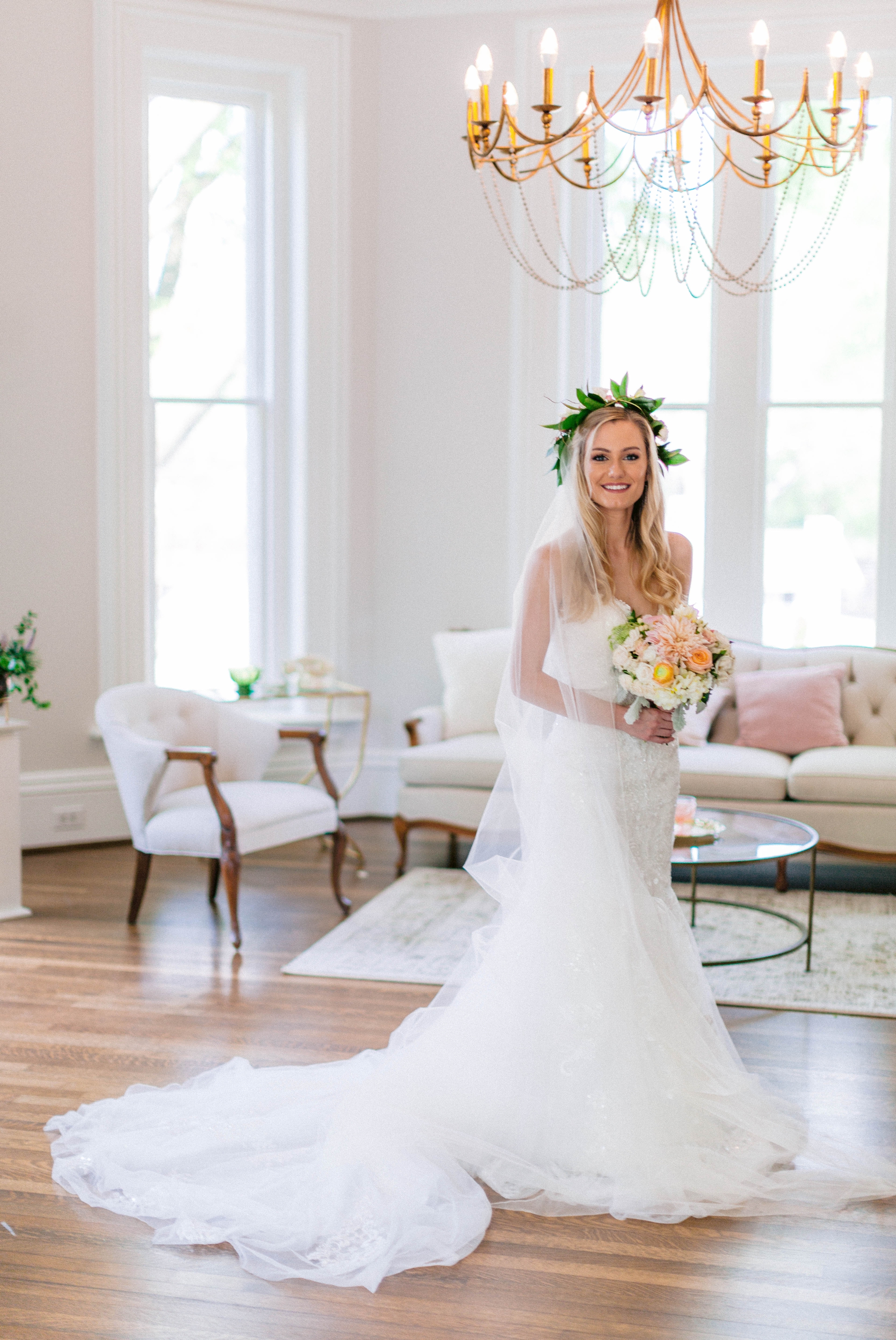  Indoor Bridal Portraits in an all white room at a luxury estate with natural light before the ceremony - Bride is wearing a Hawaiian Flower Crown and a cathedral veil in a Wedding Gown by Stella York and standing in the doorway with a golden chandel