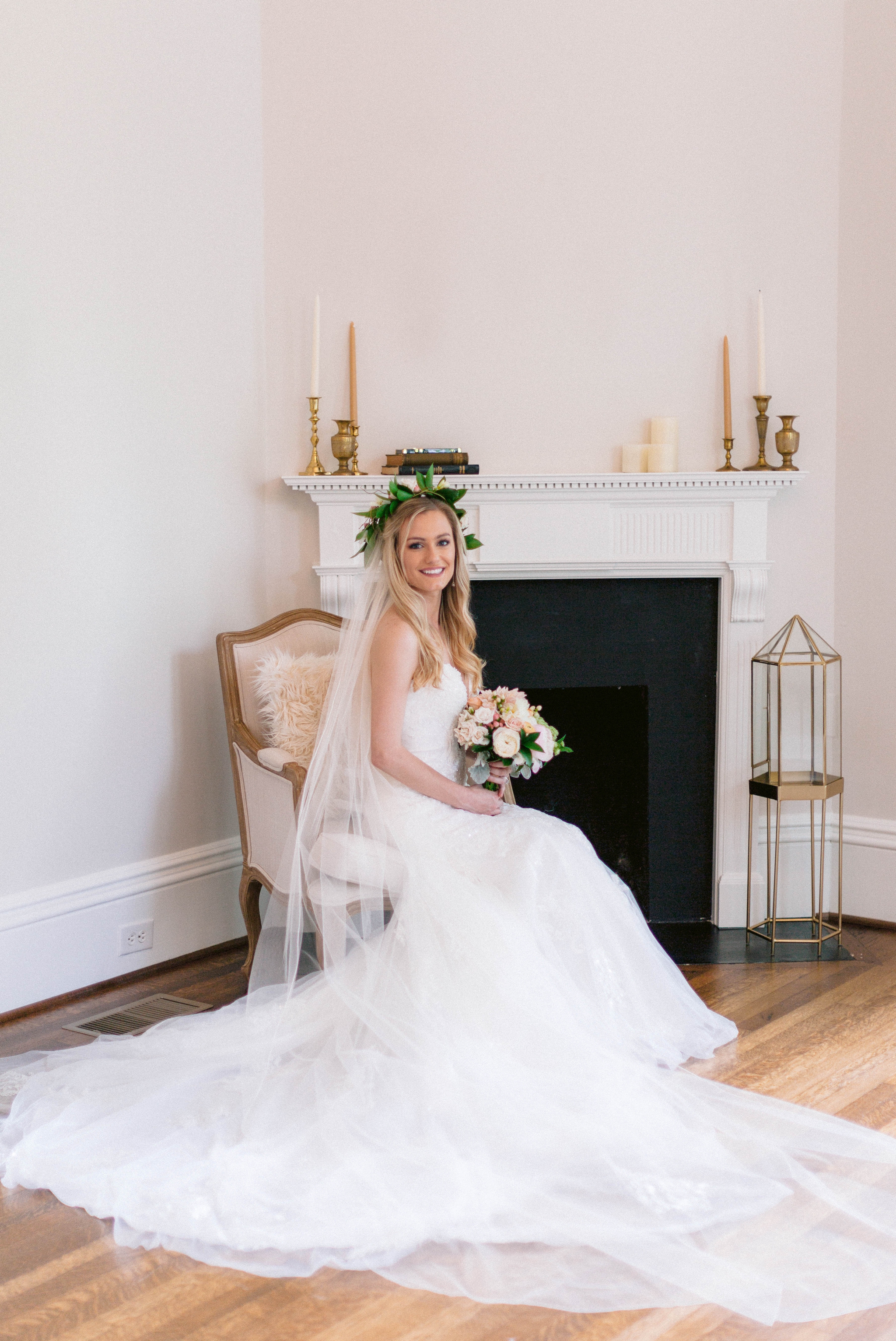  Indoor Bridal Portraits in an all white room at a luxury estate with natural light before the ceremony - Bride is wearing a Hawaiian Flower Crown and a cathedral veil in a Wedding Gown by Stella York sitting on an antique vintage chair in front of a