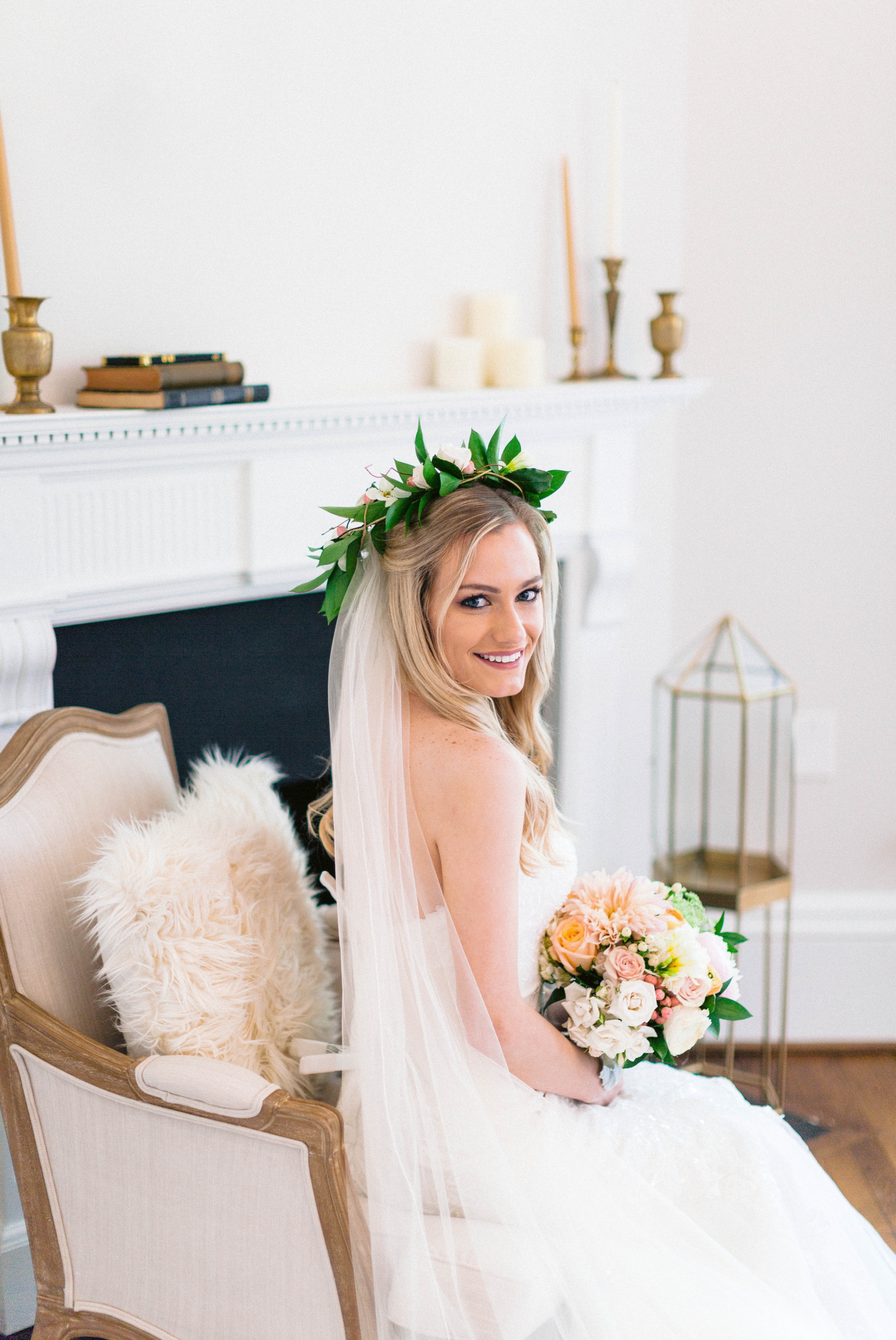  Indoor Bridal Portraits in an all white room at a luxury estate with natural light before the ceremony - Bride is wearing a Hawaiian Flower Crown and a cathedral veil in a Wedding Gown by Stella York sitting on an antique vintage chair in front of a