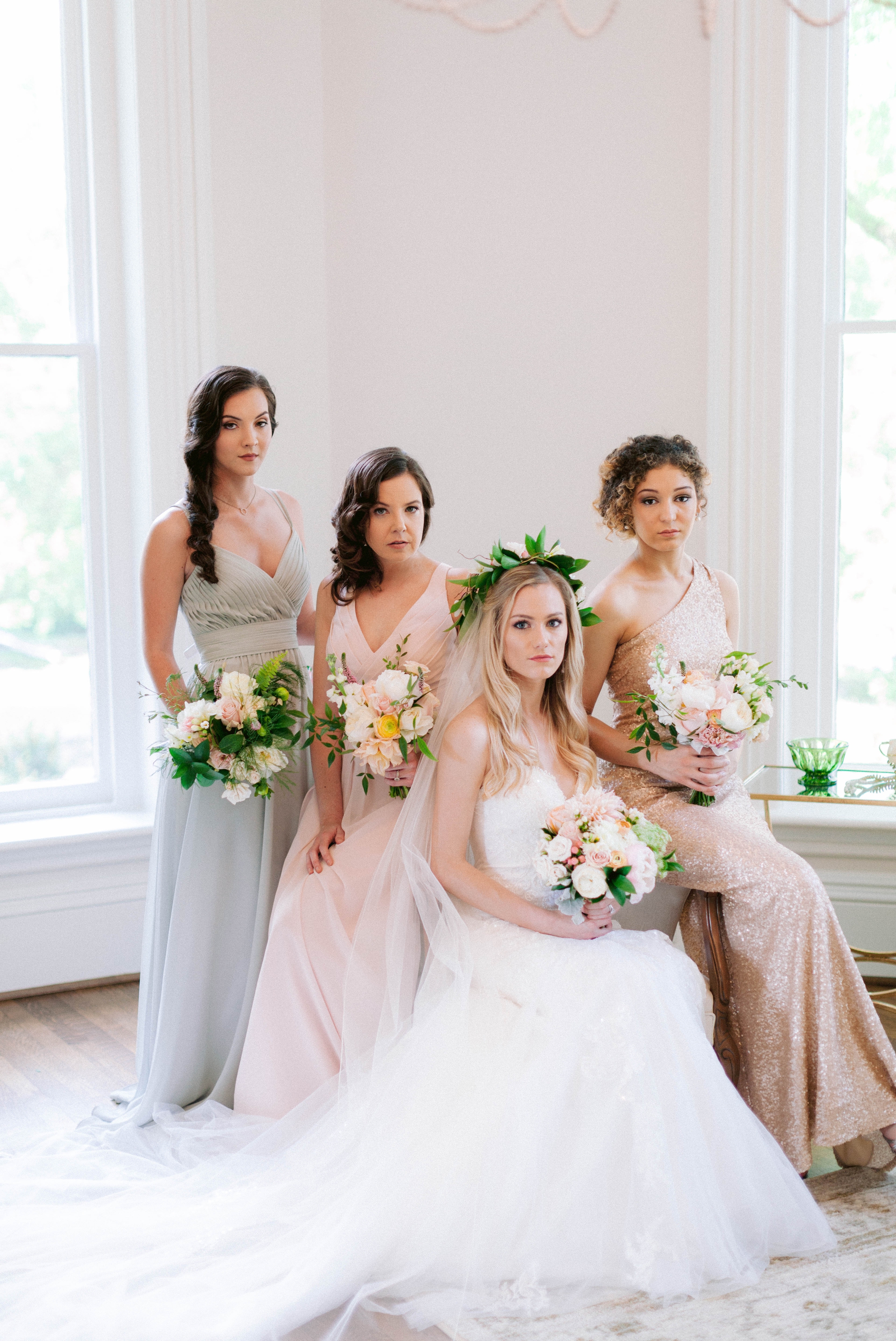  Indoor Bride + bridesmaids portraits in an all white room at a luxury estate with natural light before the ceremony sitting on a chair for an editorial shot - Bride is wearing a Hawaiian Flower Crown and a cathedral veil in a Wedding Gown by Stella 