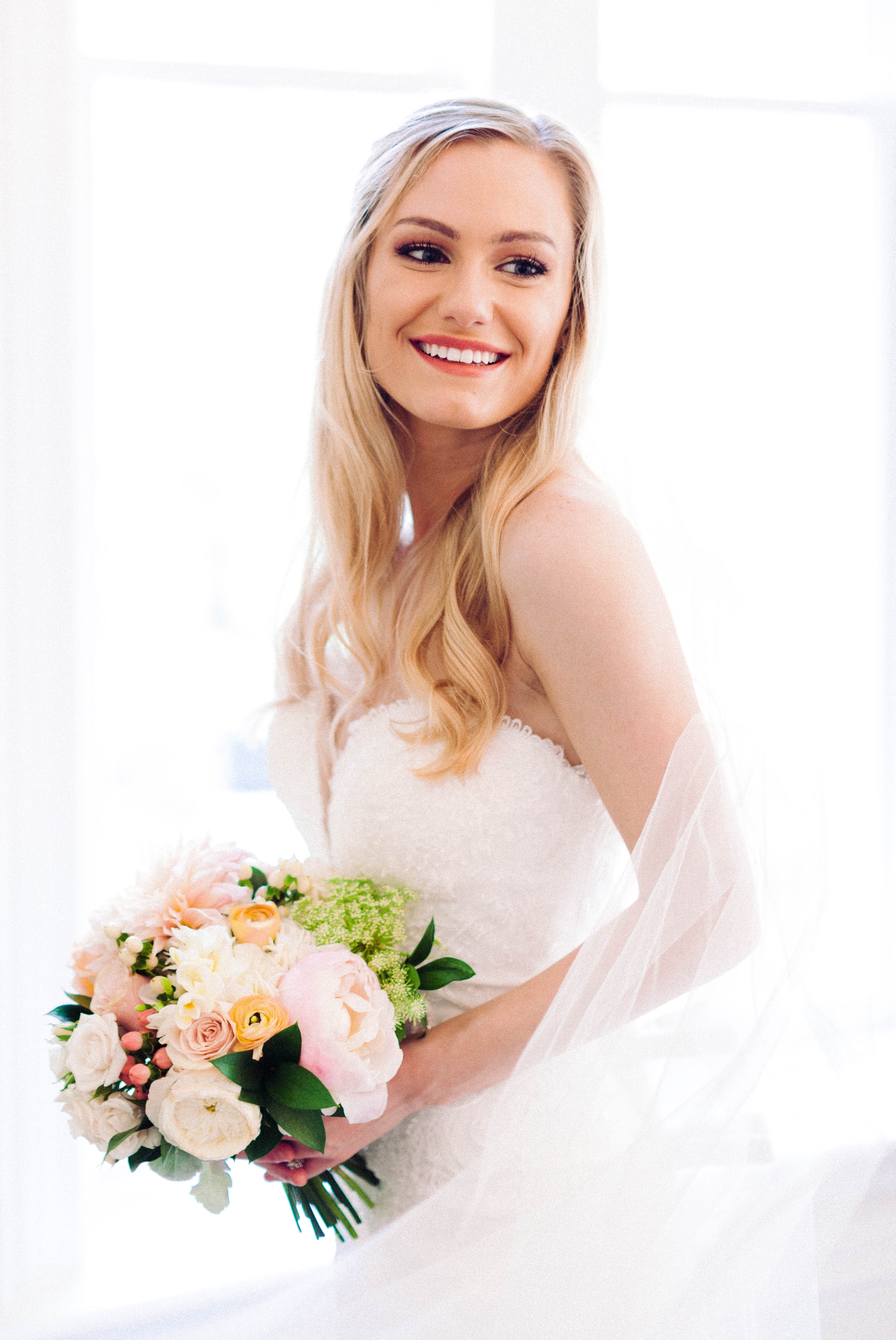  Indoor Bridal Portraits in an all white room at a luxury estate with natural light before the ceremony - Bride is wearing a Hawaiian Flower Crown and a cathedral veil in a Wedding Gown by Stella York sitting on an antique vintage chair in front of a