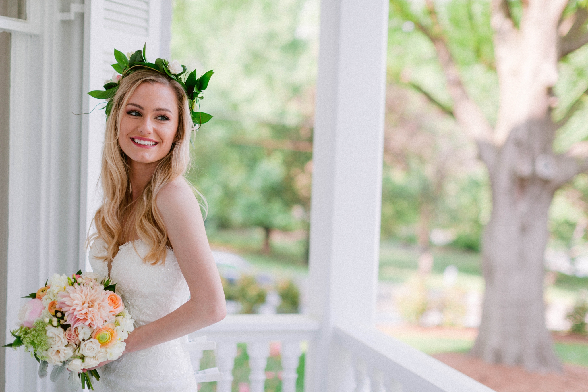  Indoor Bridal Portraits in an all white room at a luxury estate with natural light before the ceremony - Bride is wearing a Hawaiian Flower Crown in a Wedding Gown by Stella York and standing in the doorway with a golden chandelier with vintage furn