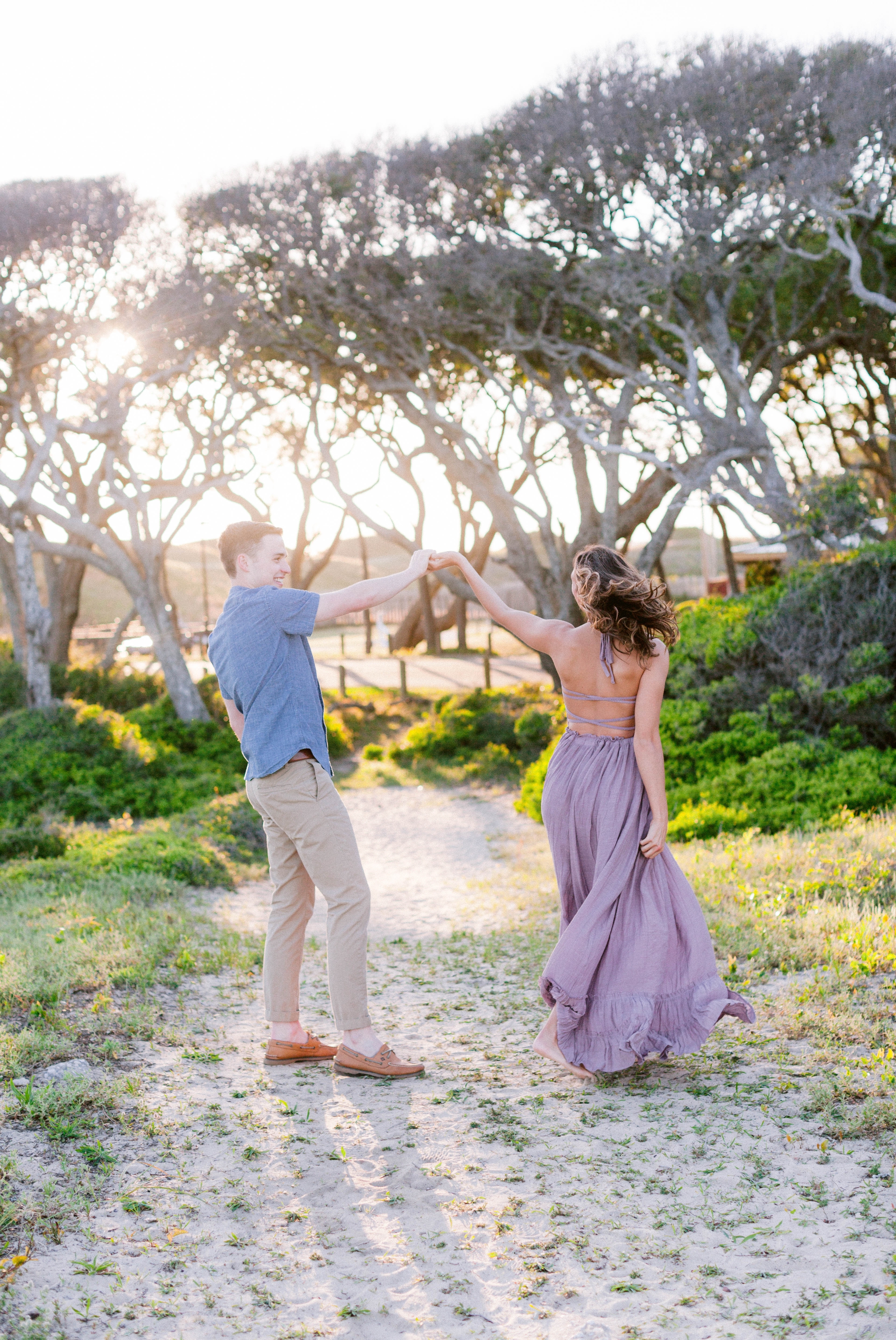  Guy dancing with girl in front of live oak trees with the sunset behind them - Woman is in a flowy pastel maxi dress - outdoor golden light session - engagement photographer in honolulu, oahu, hawaii - johanna dye photography 