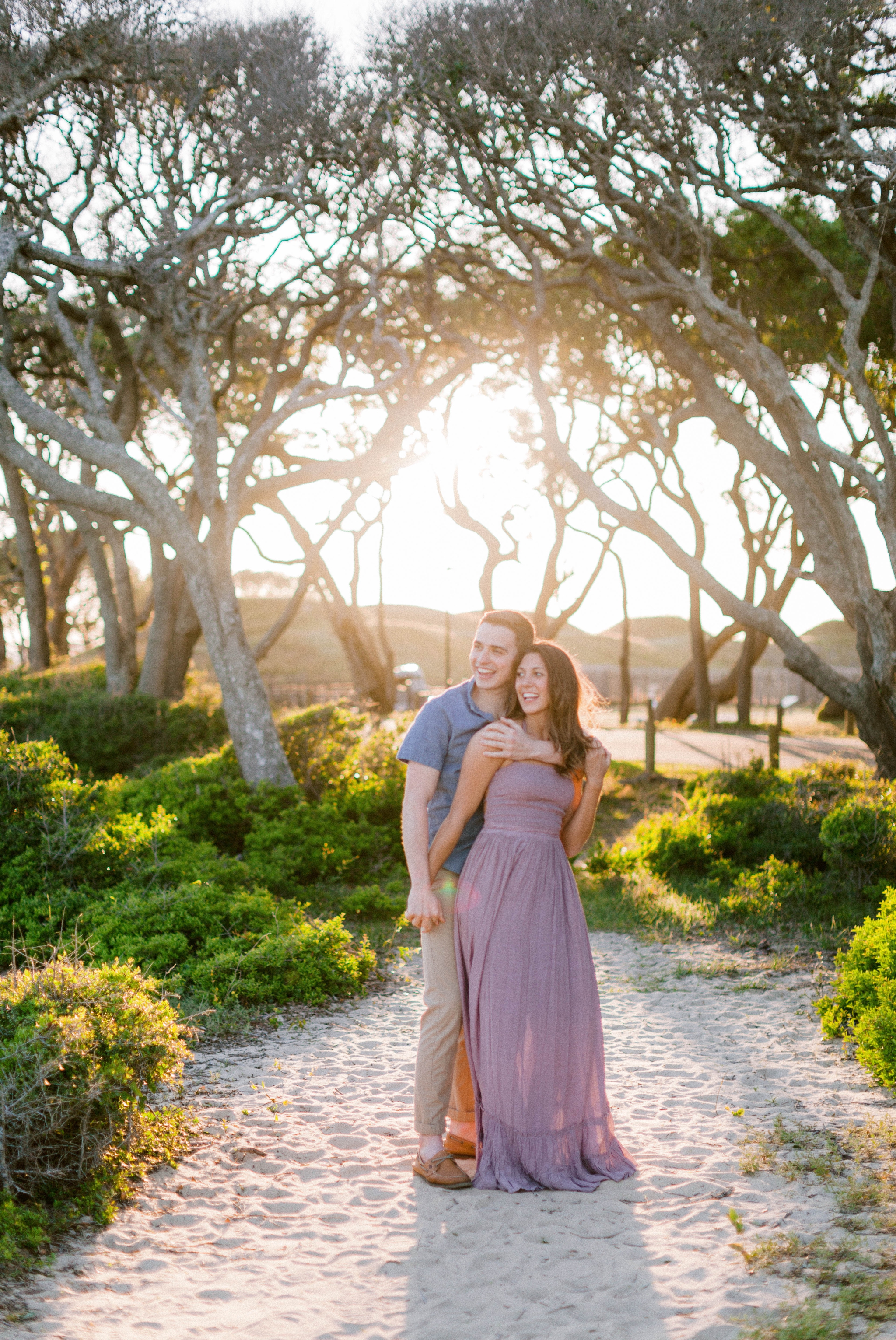  Guy dancing with girl in front of live oak trees with the sunset behind them - Woman is in a flowy pastel maxi dress - unposed and candid outdoor golden light session - engagement photographer in honolulu, oahu, hawaii - johanna dye 