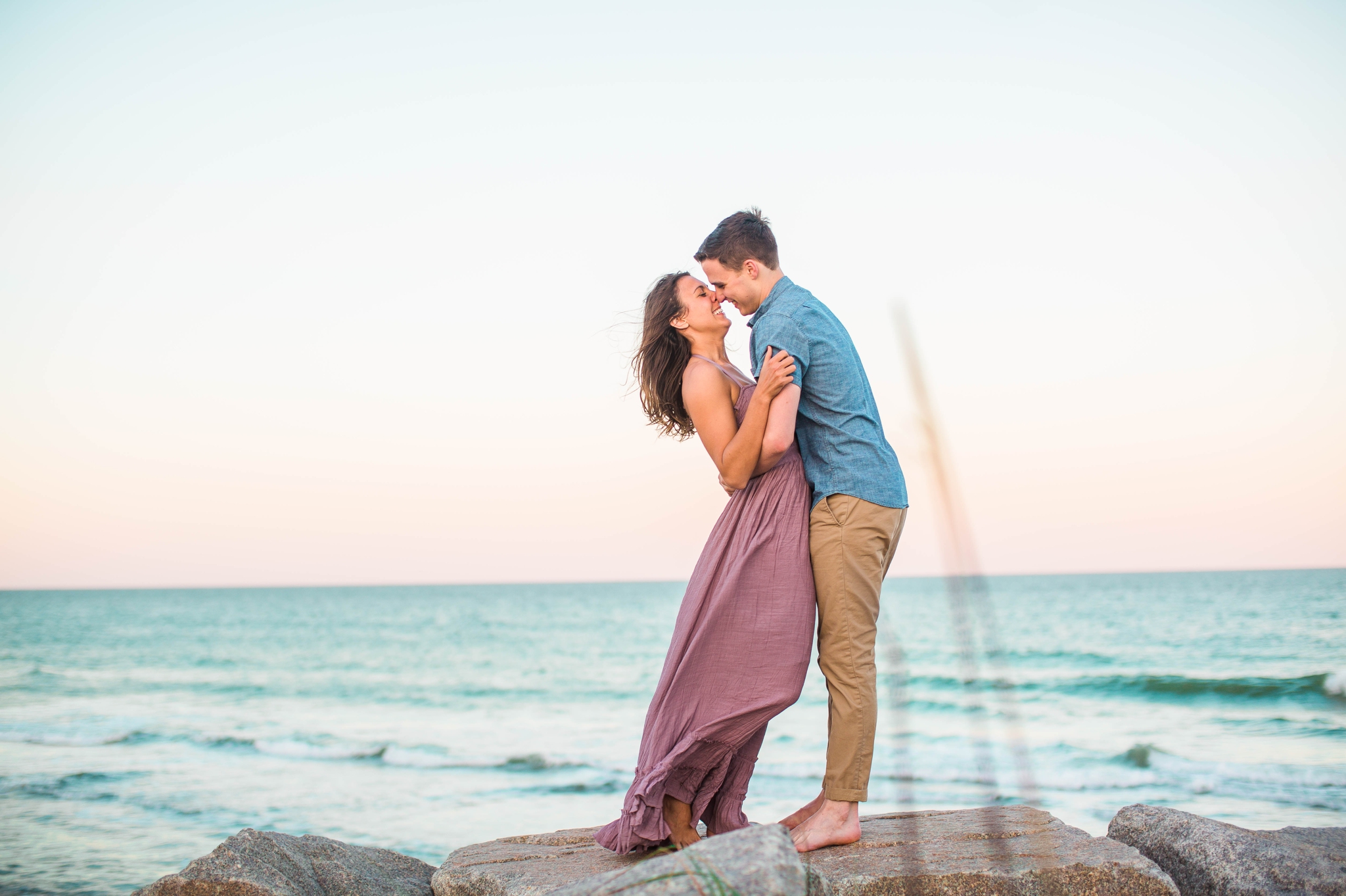  couple on the cliffs kissing - Woman is in a flowy pastel maxi dress - candid and unposed golden light session - beach engagement photographer in honolulu, oahu, hawaii - johanna dye photography 