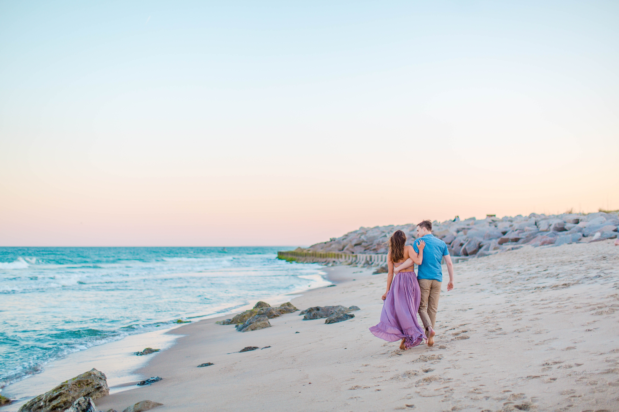 couple on the beach walking and laughing - - Woman is in a flowy pastel maxi dress - candid and unposed golden light session - beach engagement photographer in honolulu, oahu, hawaii - johanna dye photography 