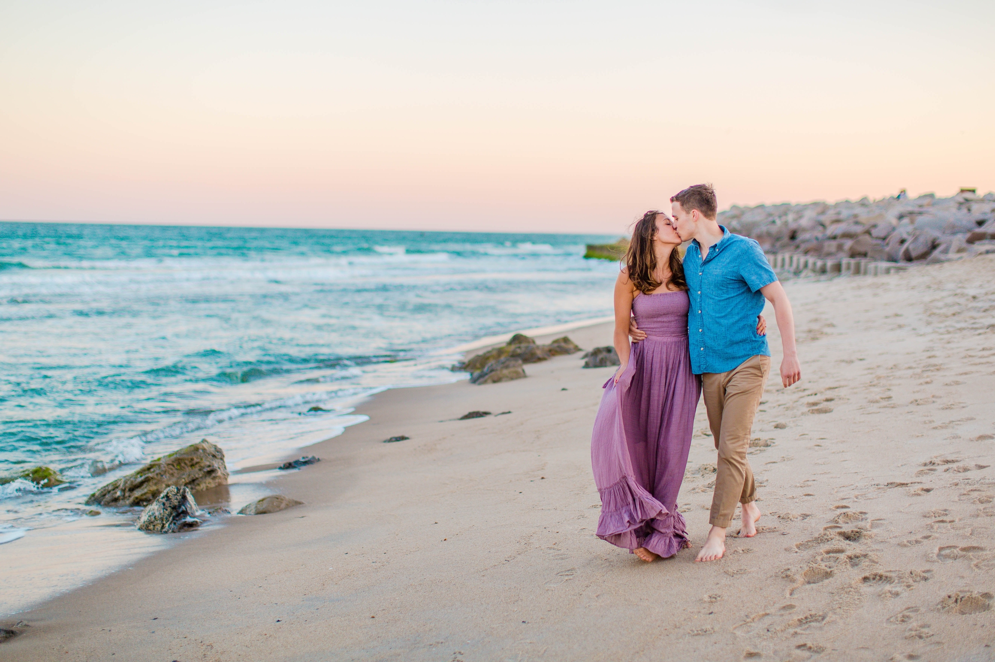 couple walking on the beach while laughing - Woman is in a flowy pastel maxi dress - candid and unposed golden light session - beach engagement photographer in honolulu, oahu, hawaii - johanna dye photography 