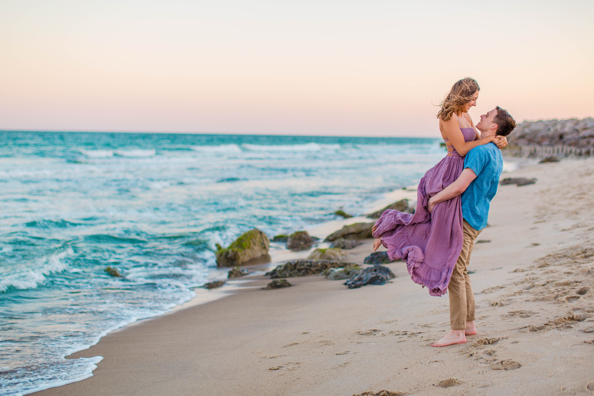  fiance picking up his girl - - Woman is in a flowy pastel maxi dress - candid and unposed golden light session - beach engagement photographer in honolulu, oahu, hawaii - johanna dye photography 