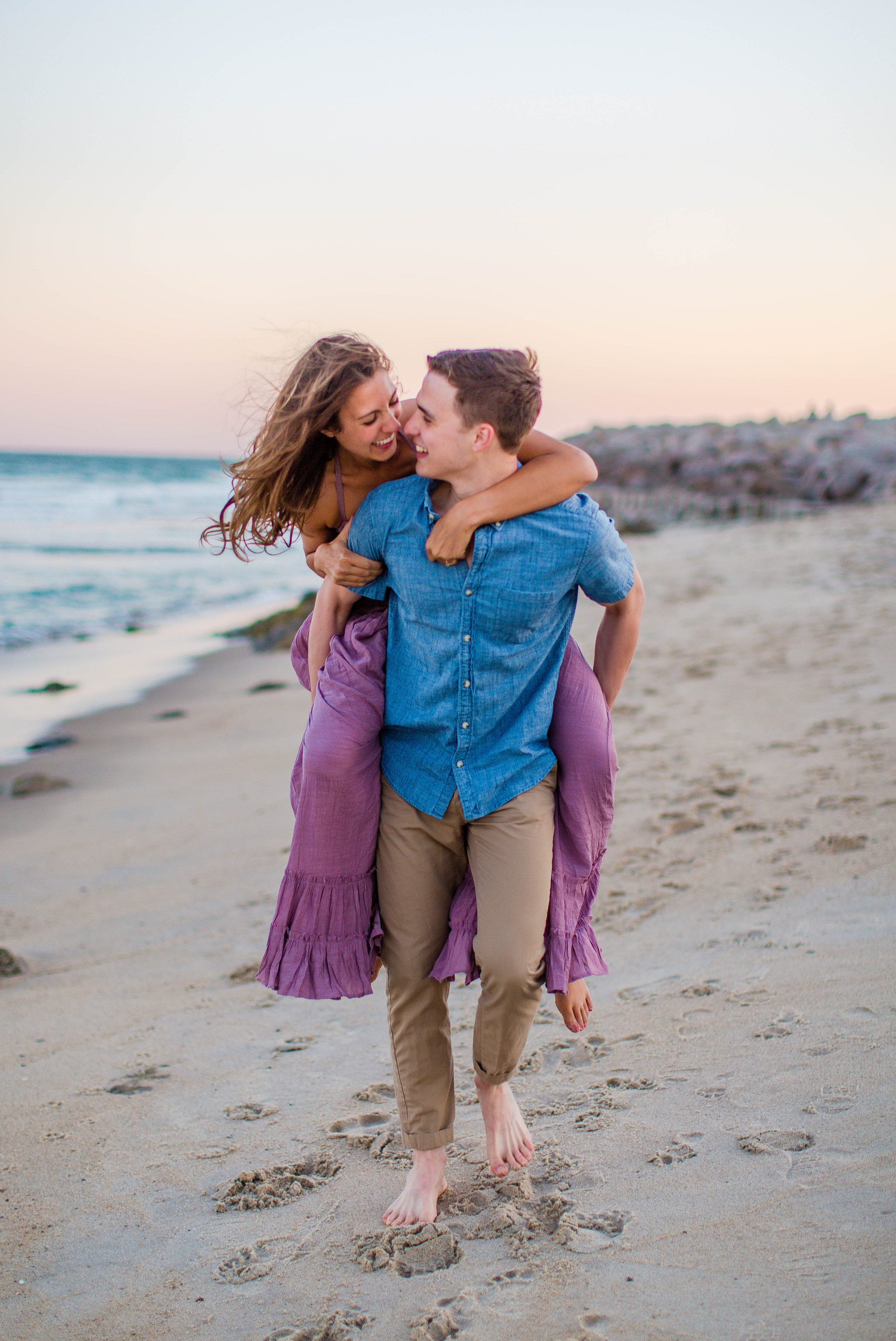  girl riding piggy back on her fiance - Woman is in a flowy pastel maxi dress - candid and unposed golden light session - beach engagement photographer in honolulu, oahu, hawaii - johanna dye photography 