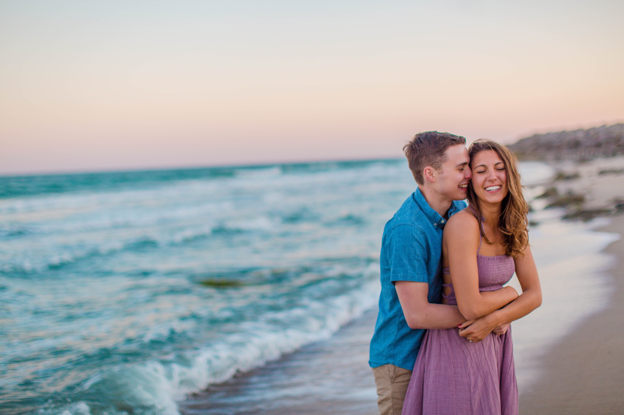  man whispering into his fiances ear - - Woman is in a flowy pastel maxi dress - candid and unposed golden light session - beach engagement photographer in honolulu, oahu, hawaii - johanna dye photography 