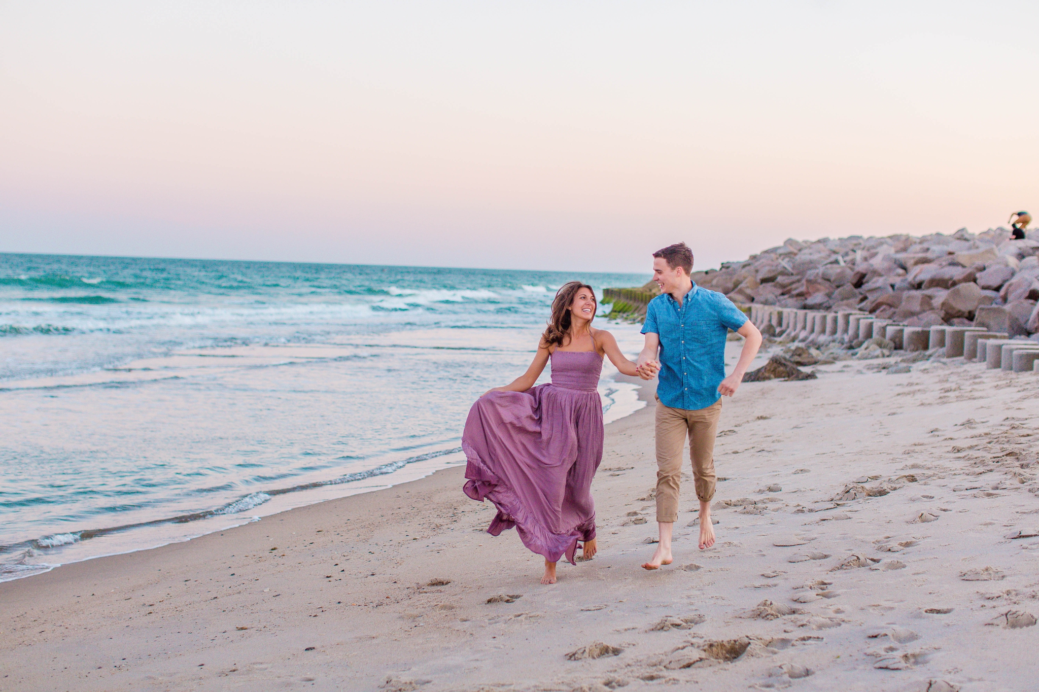  man and woman running in the sand - - Woman is in a flowy pastel maxi dress - candid and unposed golden light session - beach engagement photographer in honolulu, oahu, hawaii - johanna dye photography 